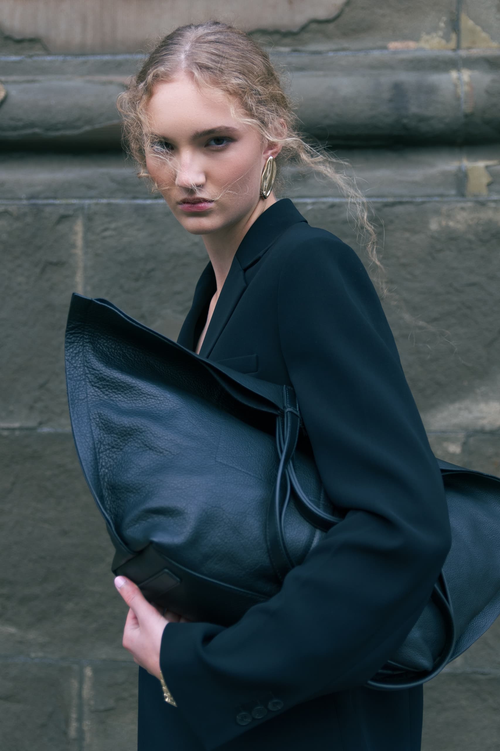 Fashionable woman in a black coat holding a large leather handbag.