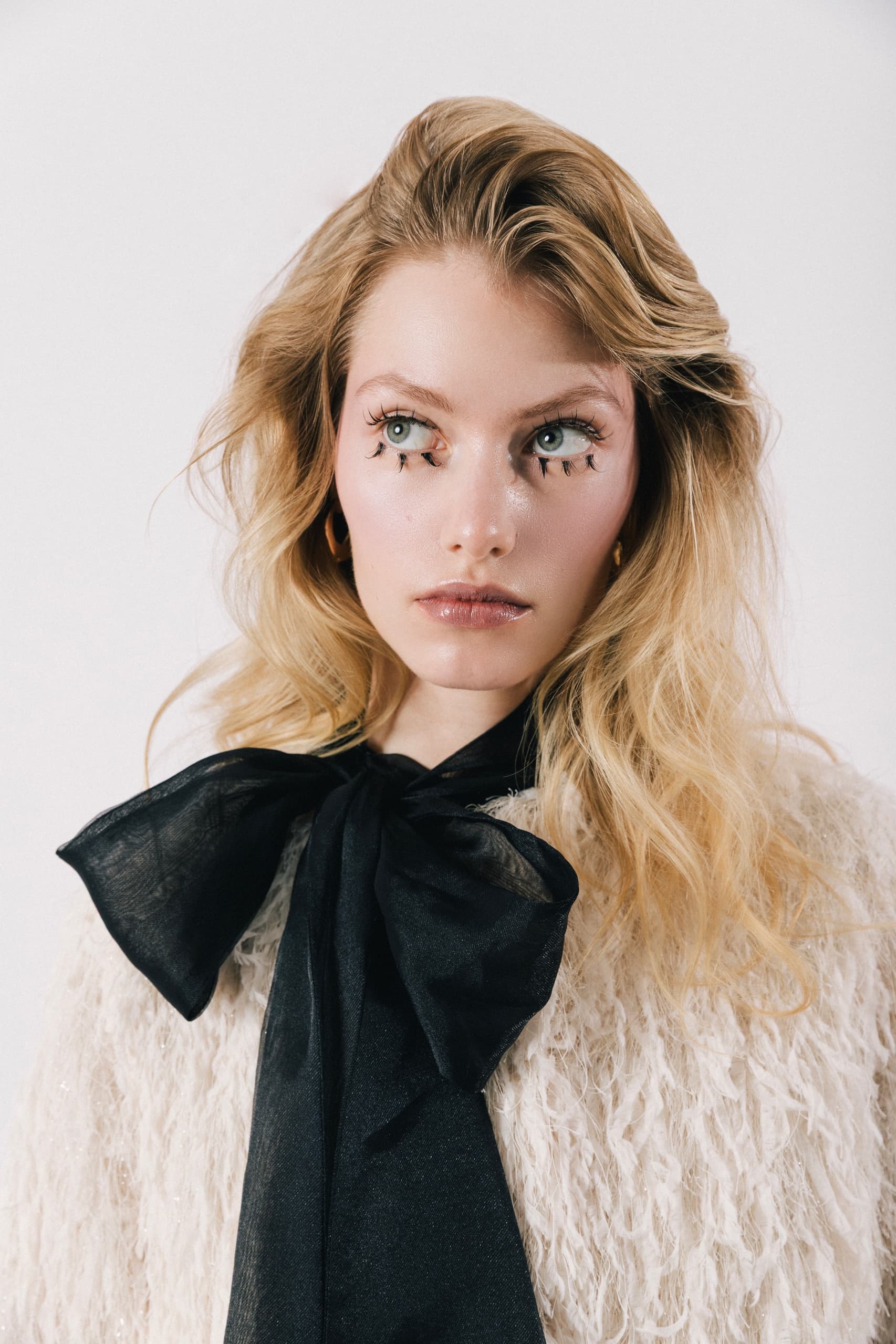 Blonde model with a large black bow tie and artistic eye makeup, stylish fashion look.