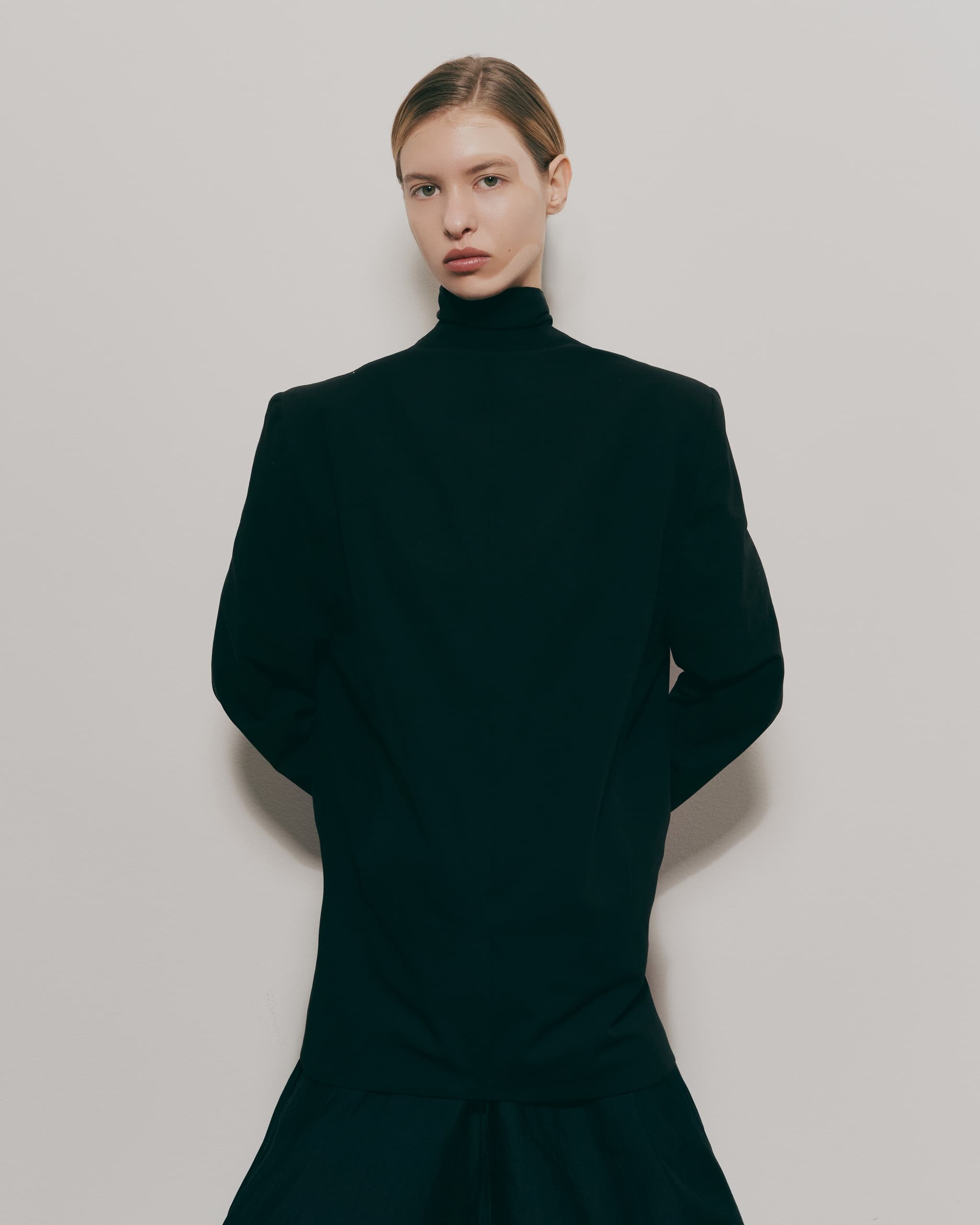 Stylish person in black turtleneck posing against a plain background.