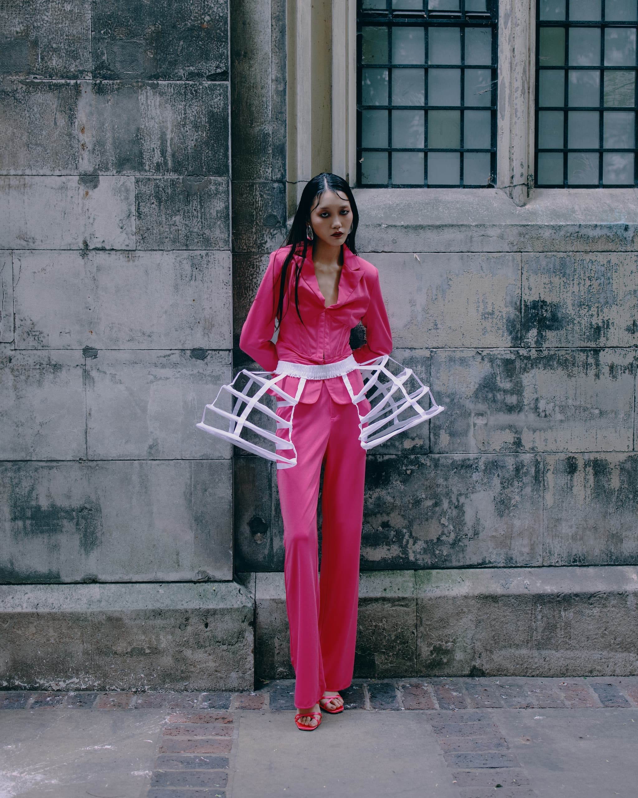 Person in pink outfit with cage design against an old stone wall.