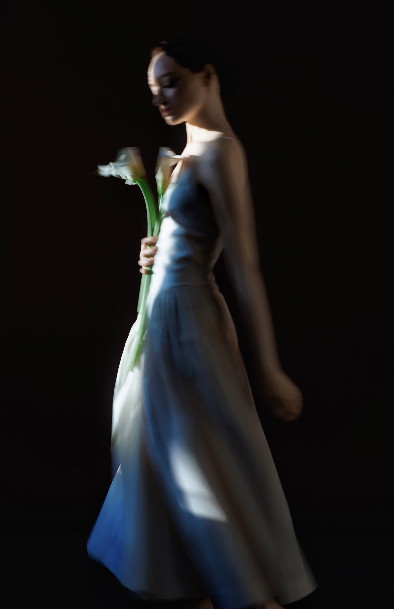 Elegant woman holding flowers, wearing a flowing dress in artistic low light.