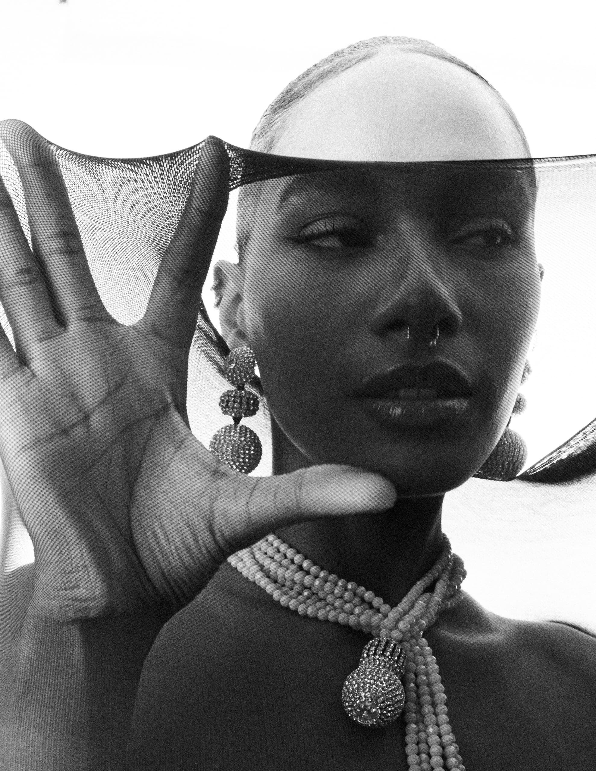 Elegant woman poses in artistic black veil and jewelry, black and white portrait.
