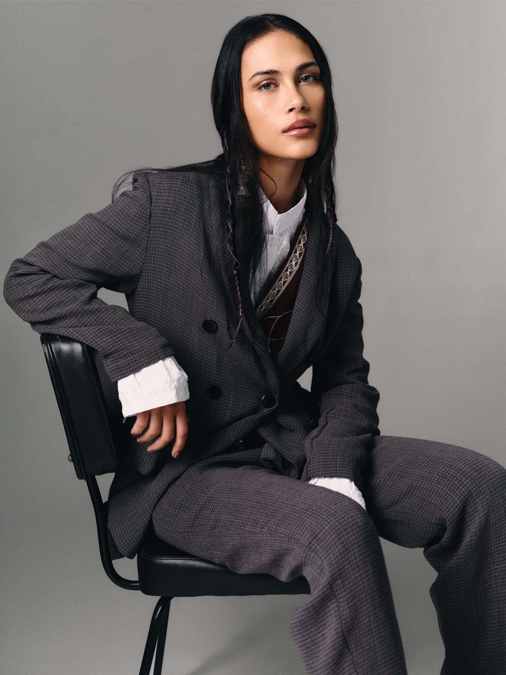Stylish woman in a gray suit sitting confidently on a chair.