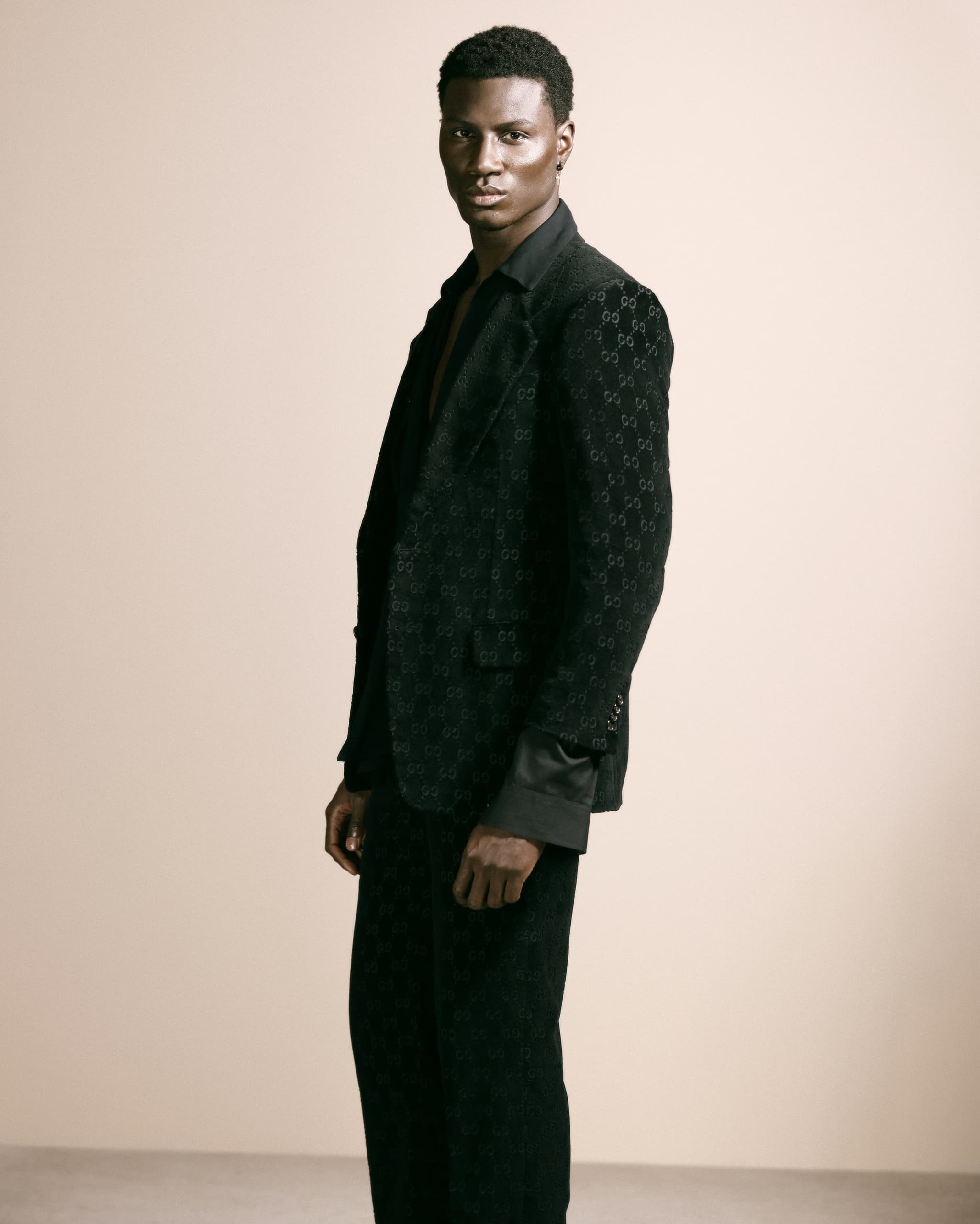 Man in an elegant black suit standing against a neutral background.