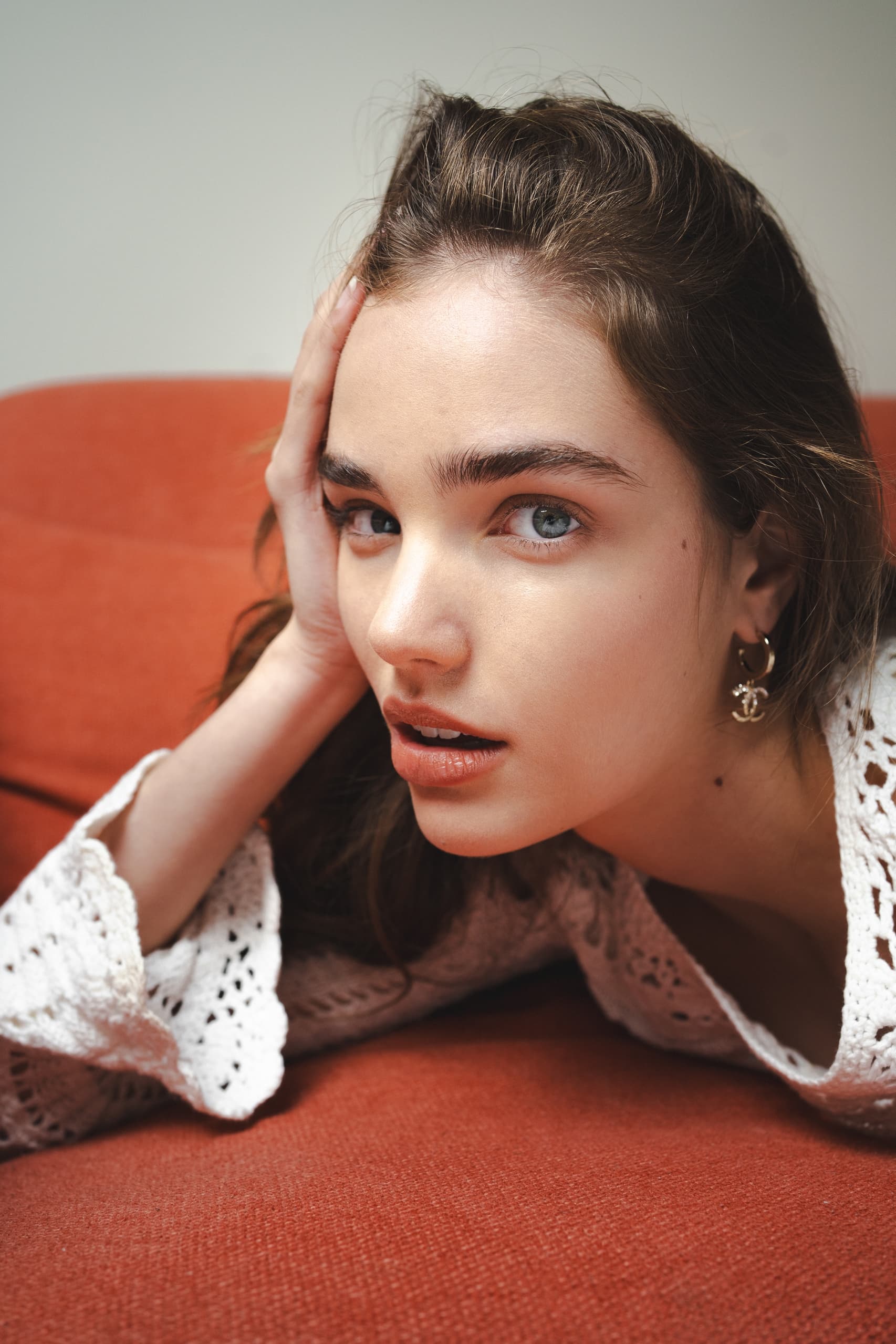 Woman in white lace top, reclined on a red sofa, looking towards the camera.