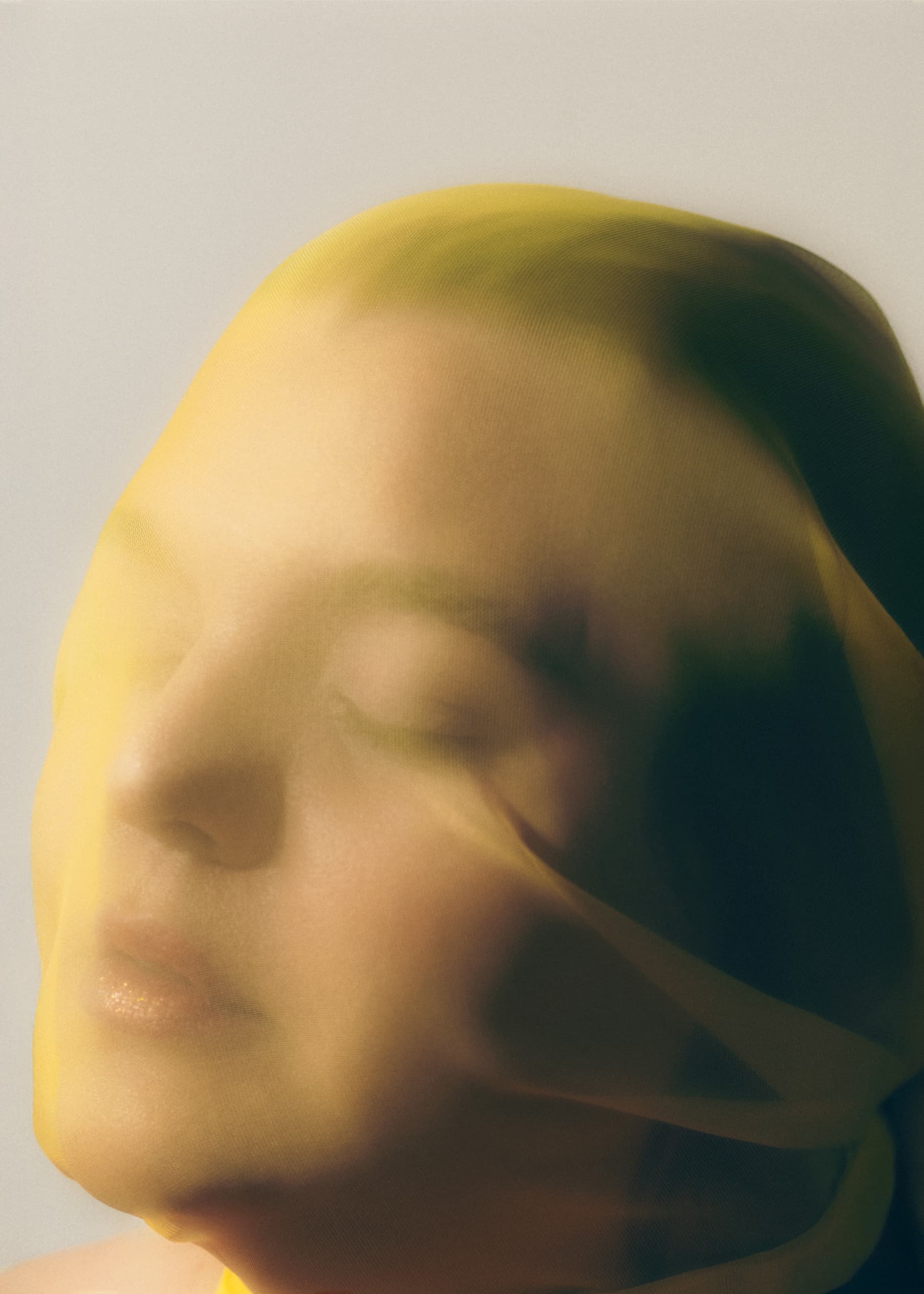 Artistic portrait of face covered in yellow translucent fabric.