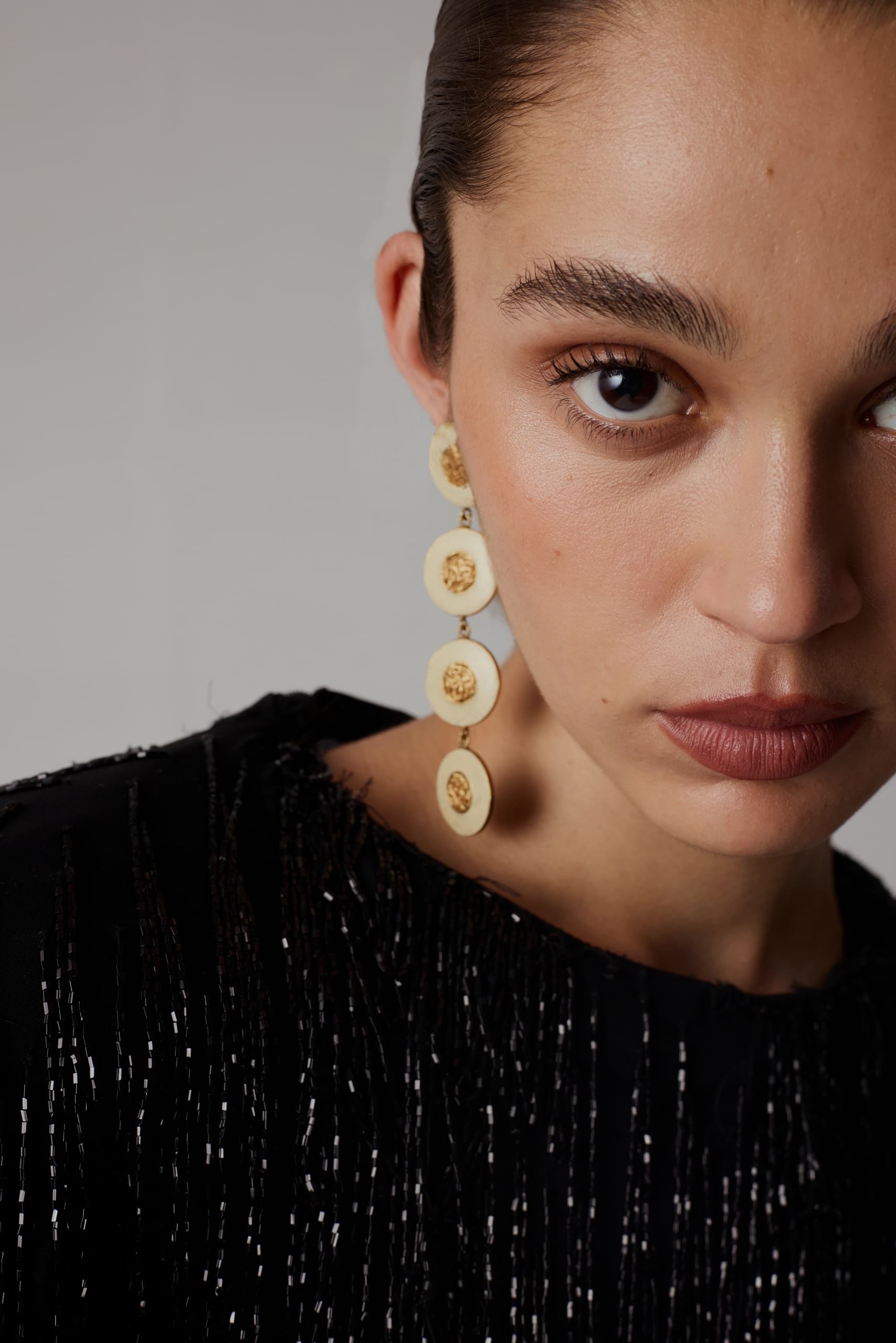 Close-up of elegant dangling earrings against a textured black outfit.