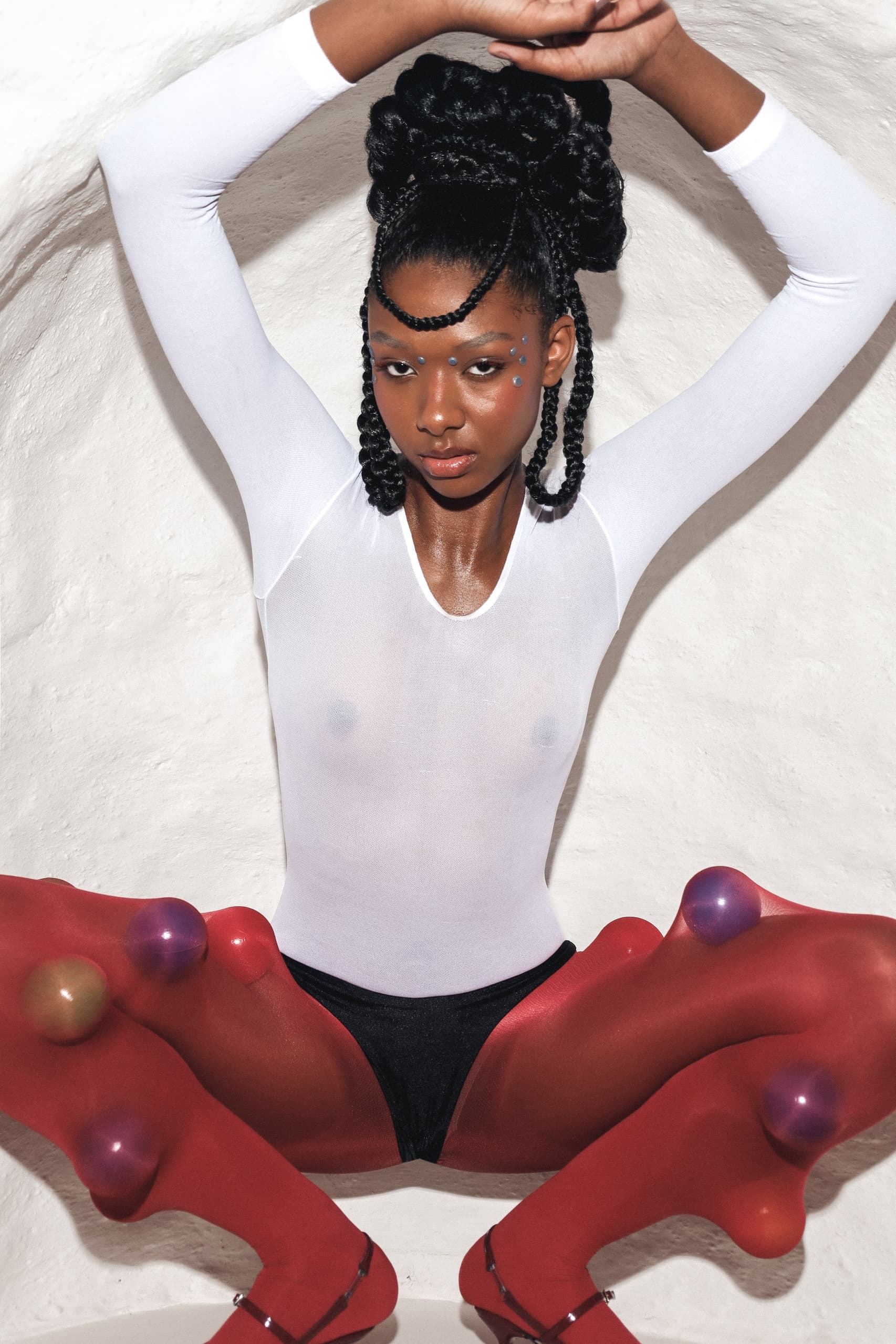 Fashion-forward model in white bodysuit and red tights with bold accessories.