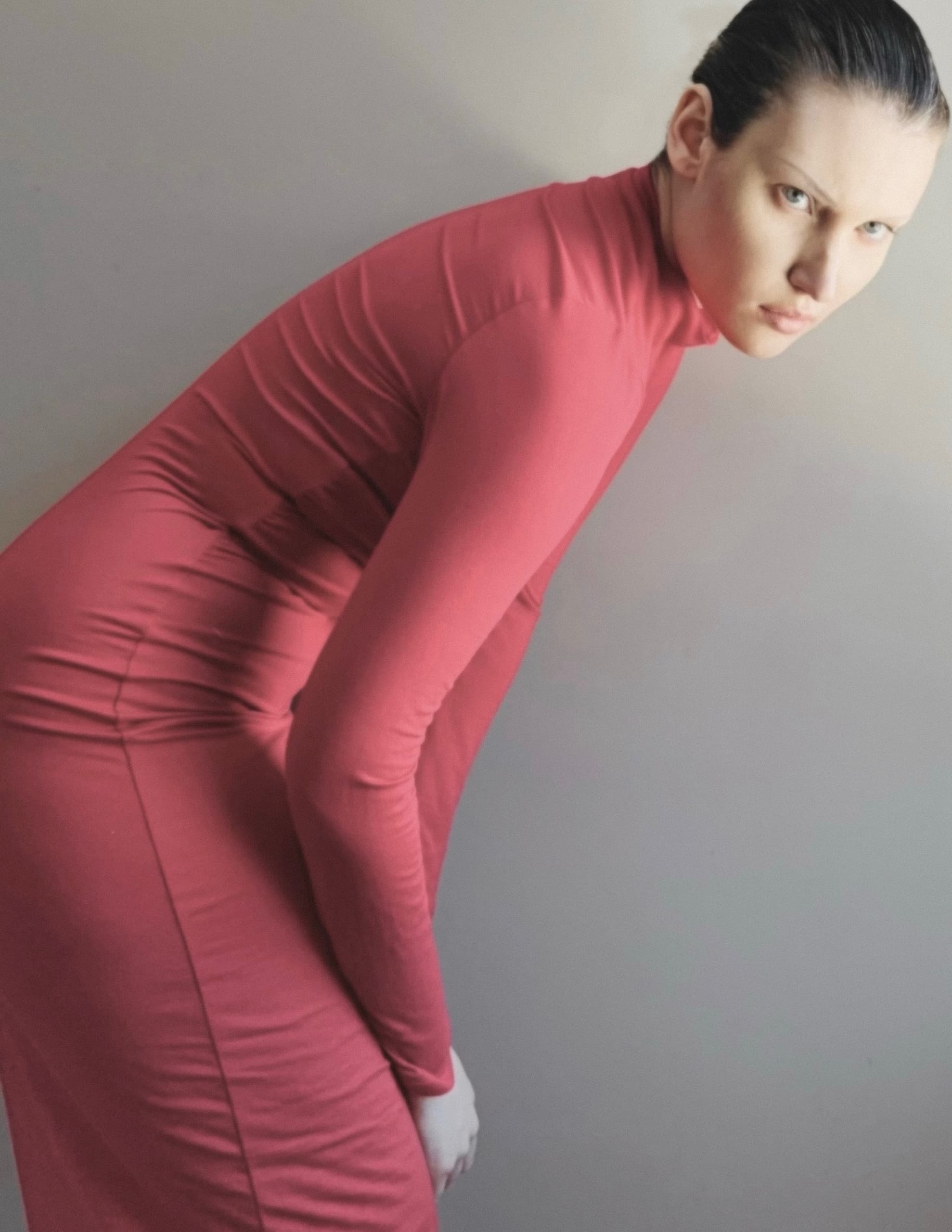 Person in pink form-fitting dress posing against minimalistic background.