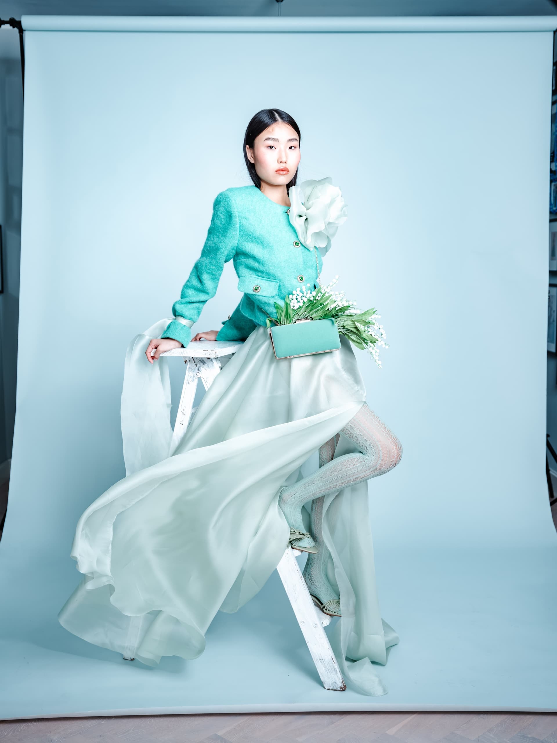 Fashion model in elegant teal outfit on studio backdrop with floral accents.