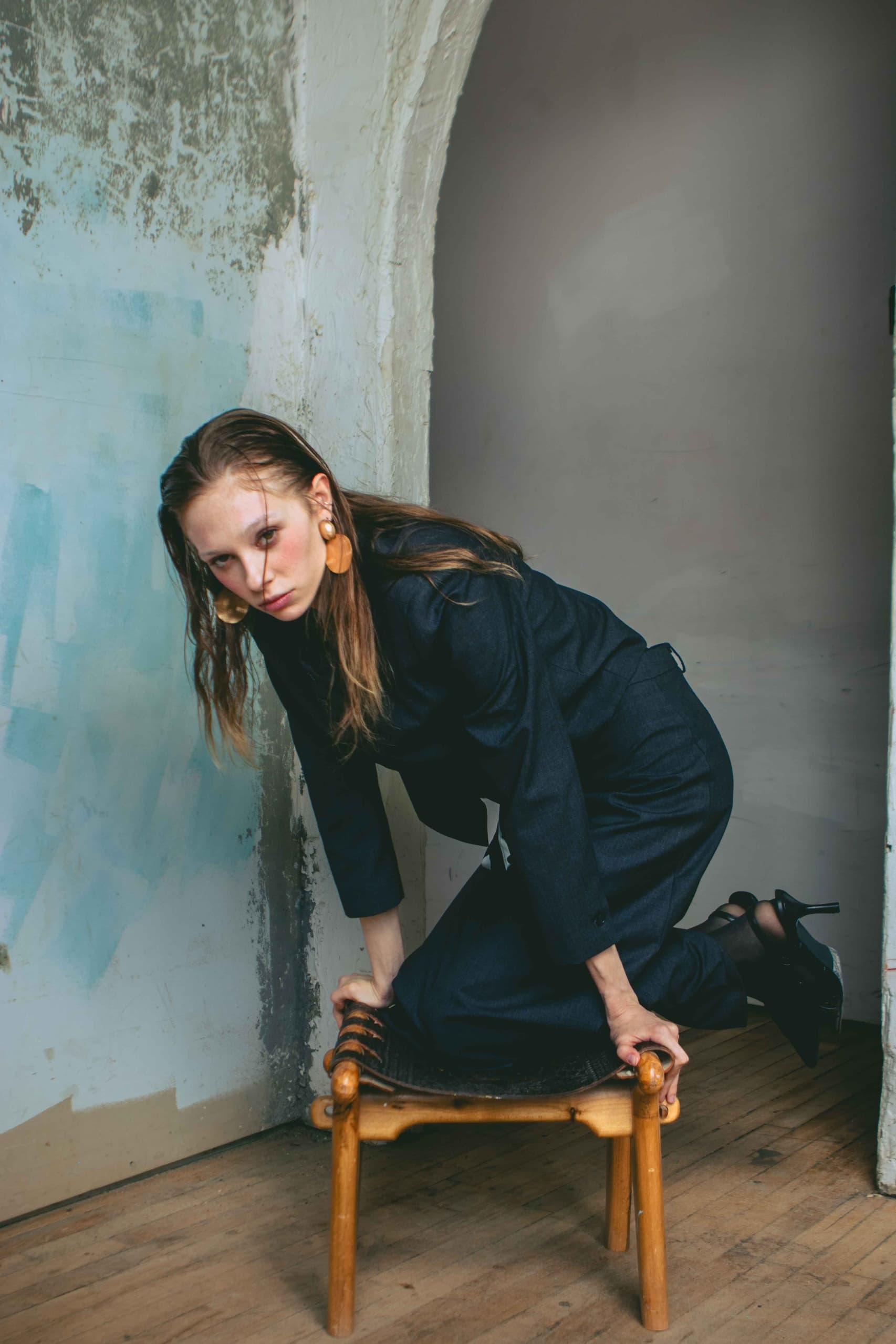 Fashionable woman poses on chair in stylish outfit in minimalistic room.