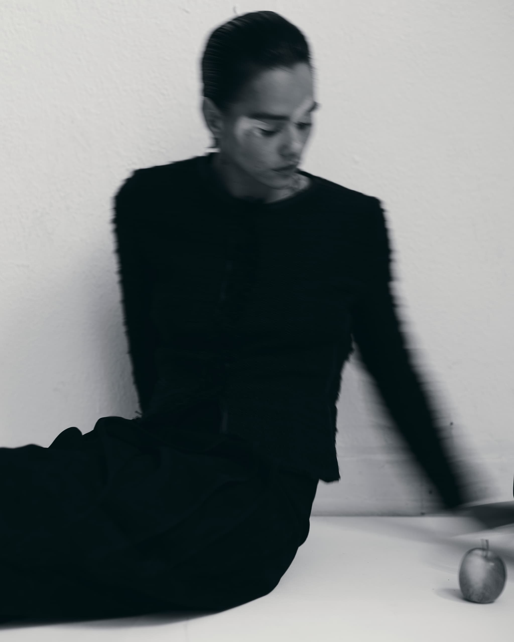 Blurry artistic photo of a person in black clothes beside a small apple on the floor.