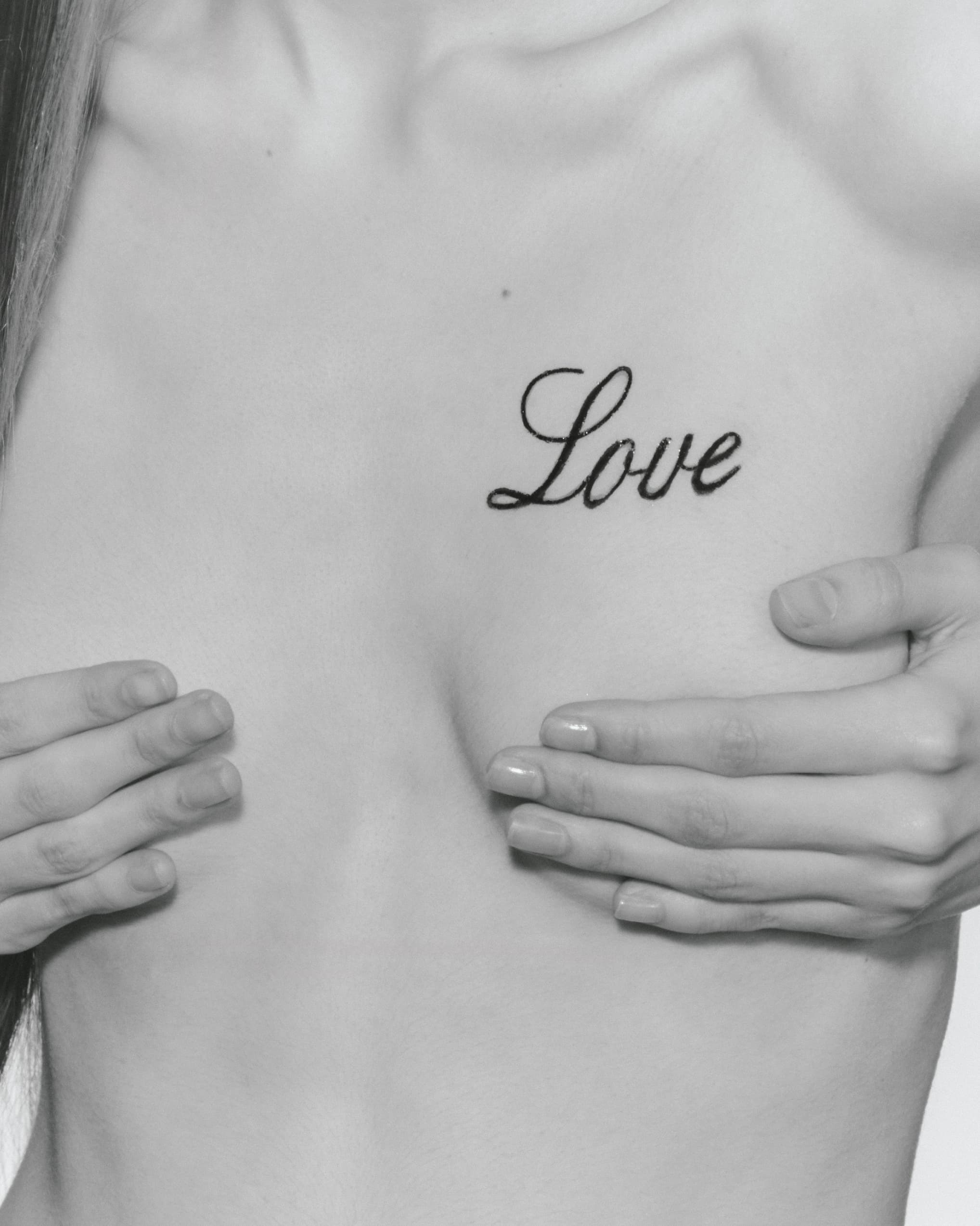Love tattoo on chest, monochrome close-up, hands covering torso