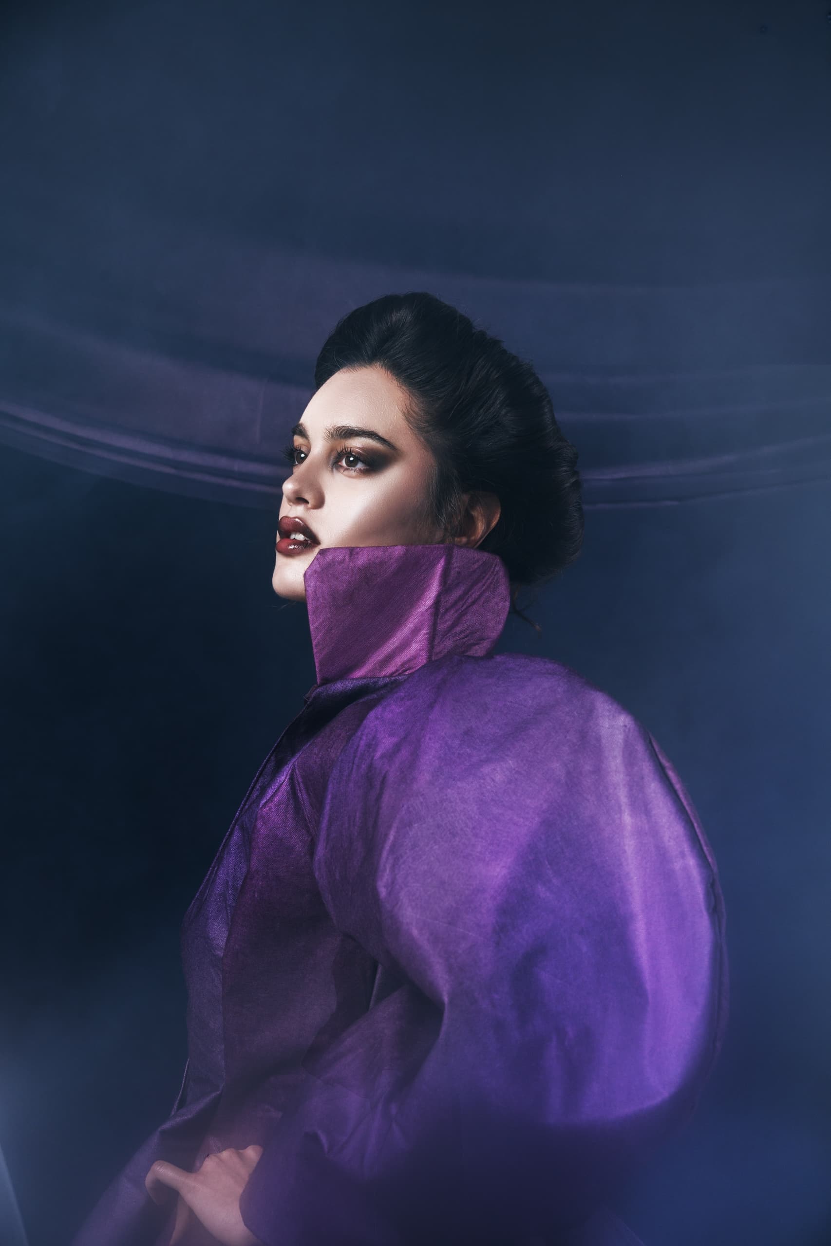 Fashion model in dramatic purple outfit with smoky background.