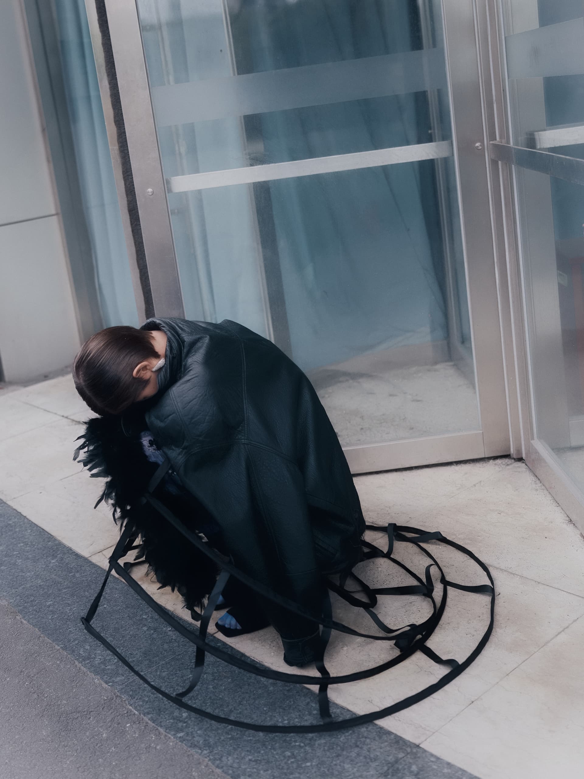 Person in black outfit crouched near glass door with circular straps on concrete floor.
