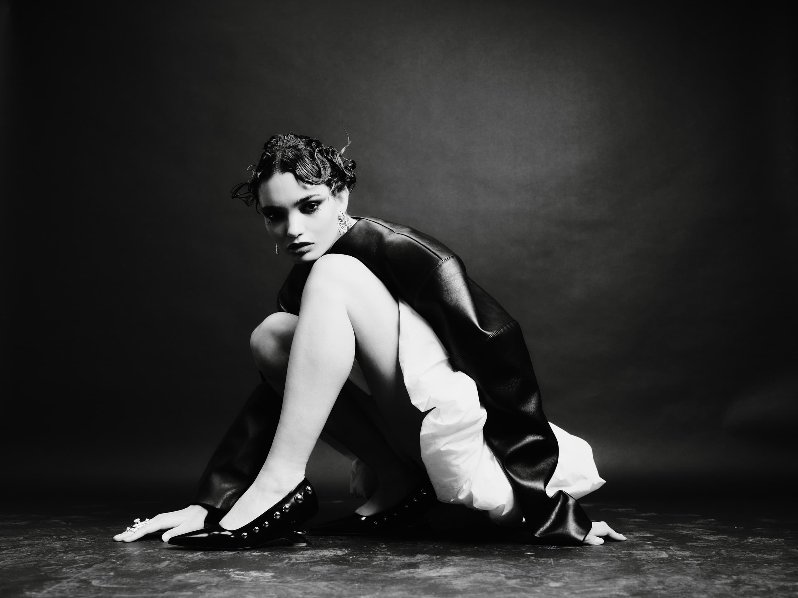 Black and white fashion portrait of person in stylish outfit, crouching pose.