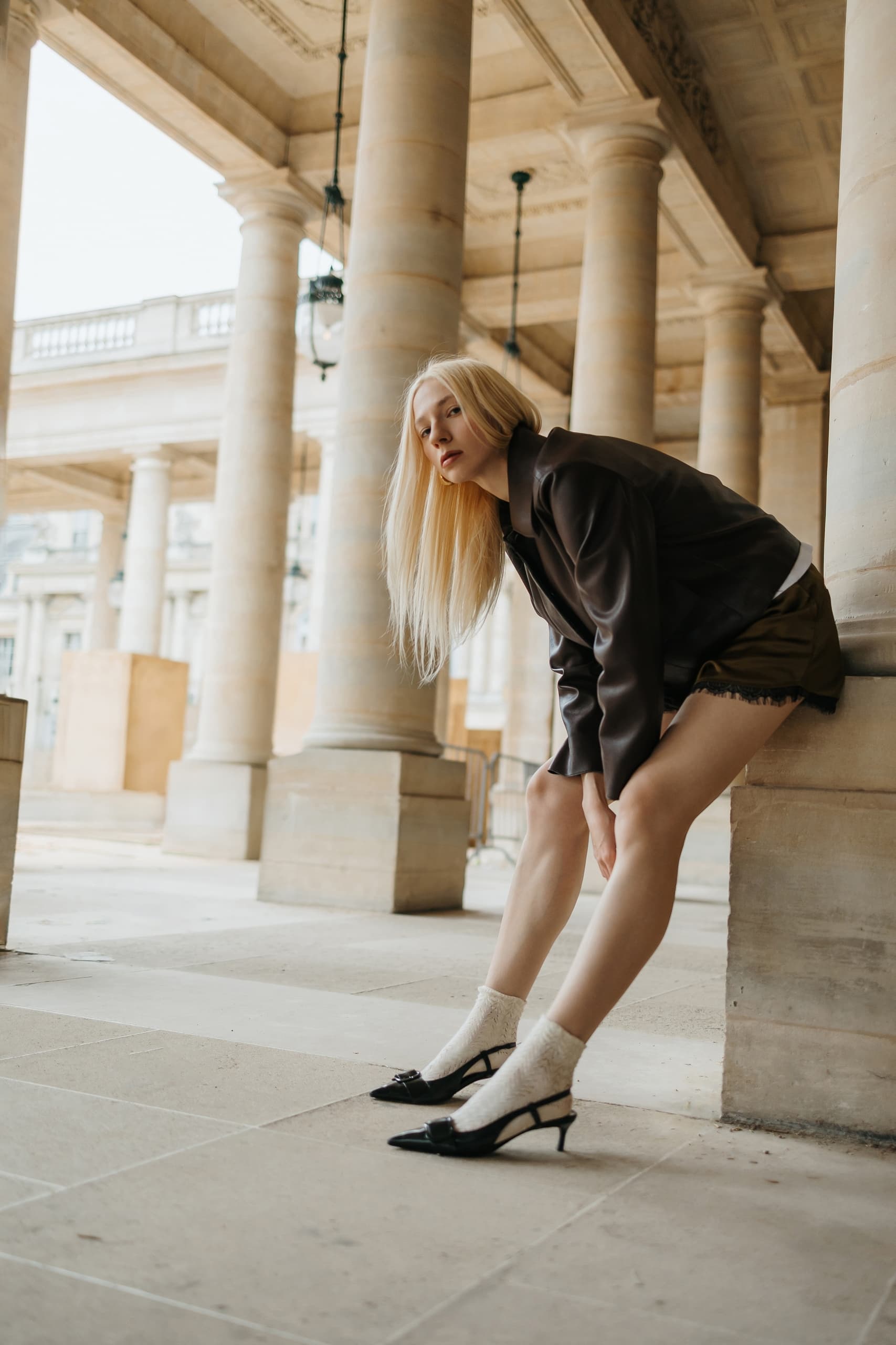 Fashionable woman in stylish outfit posing among stone columns.