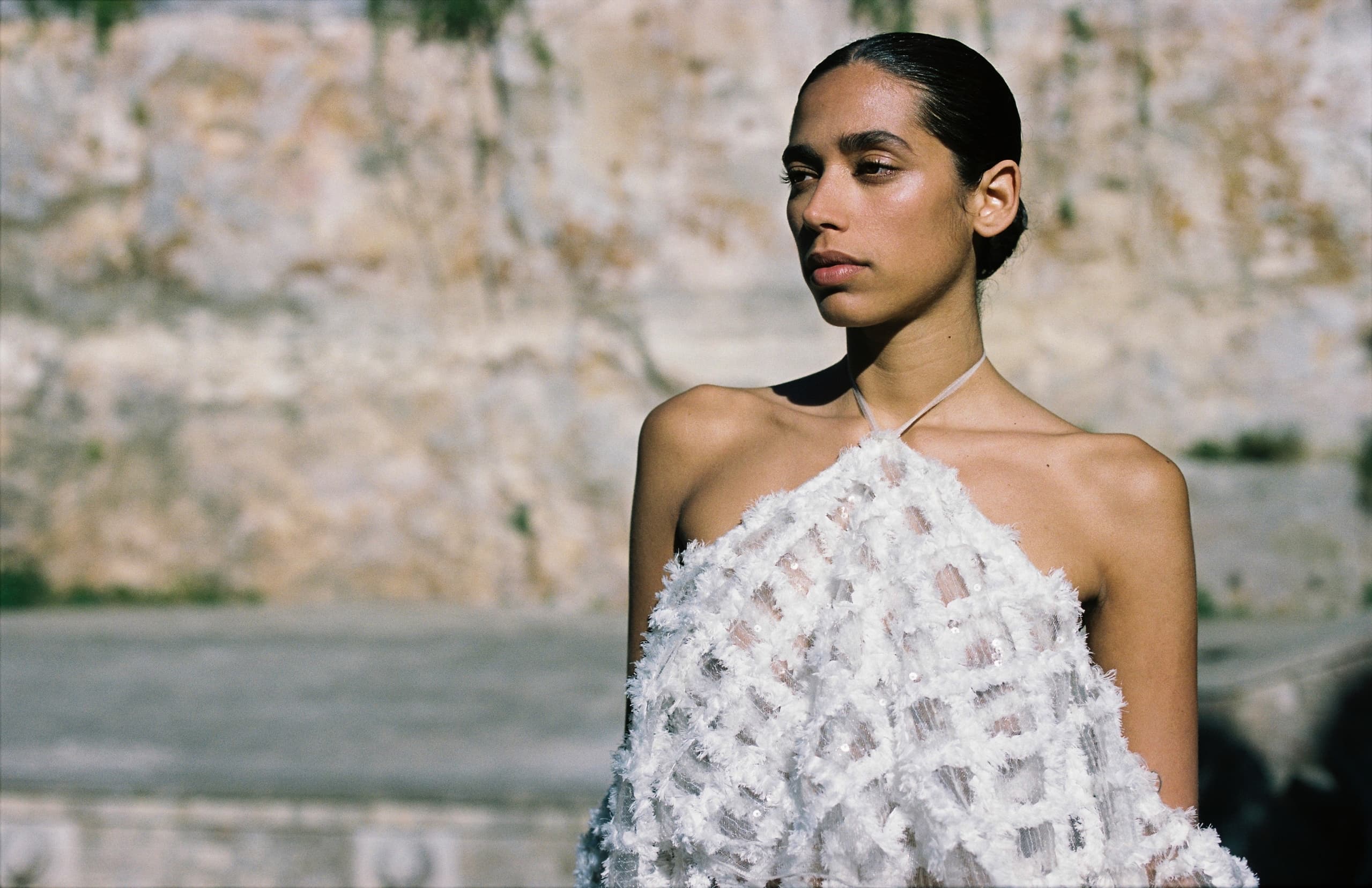 Person in white textured outfit against a stone wall, showcasing modern fashion outdoors.