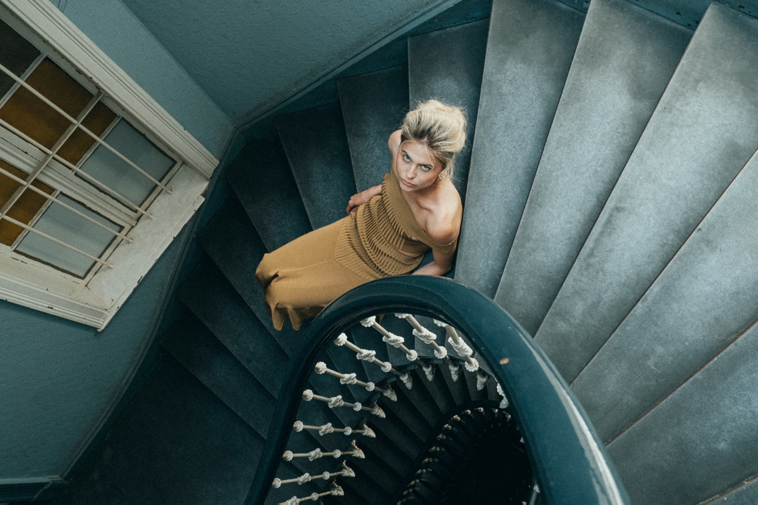 Woman in brown dress sitting on spiral staircase, viewed from above.