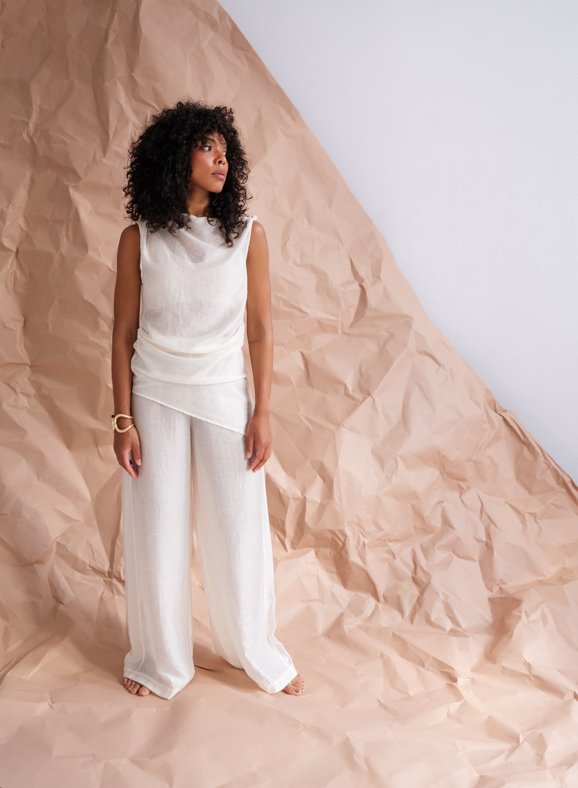 Woman in stylish white outfit poses on crumpled paper background.