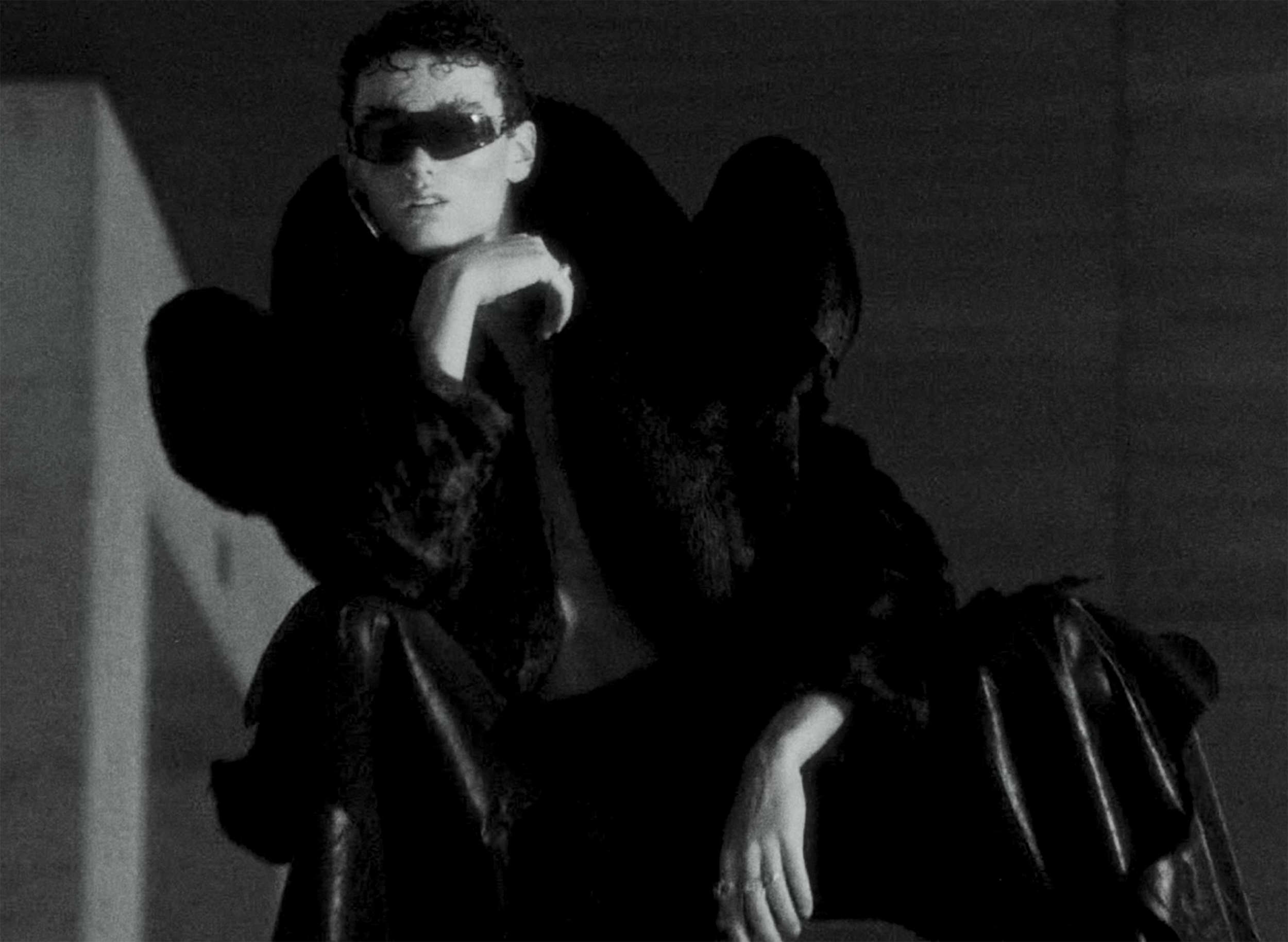 Fashion model in dark fur coat and sunglasses, striking a confident pose.