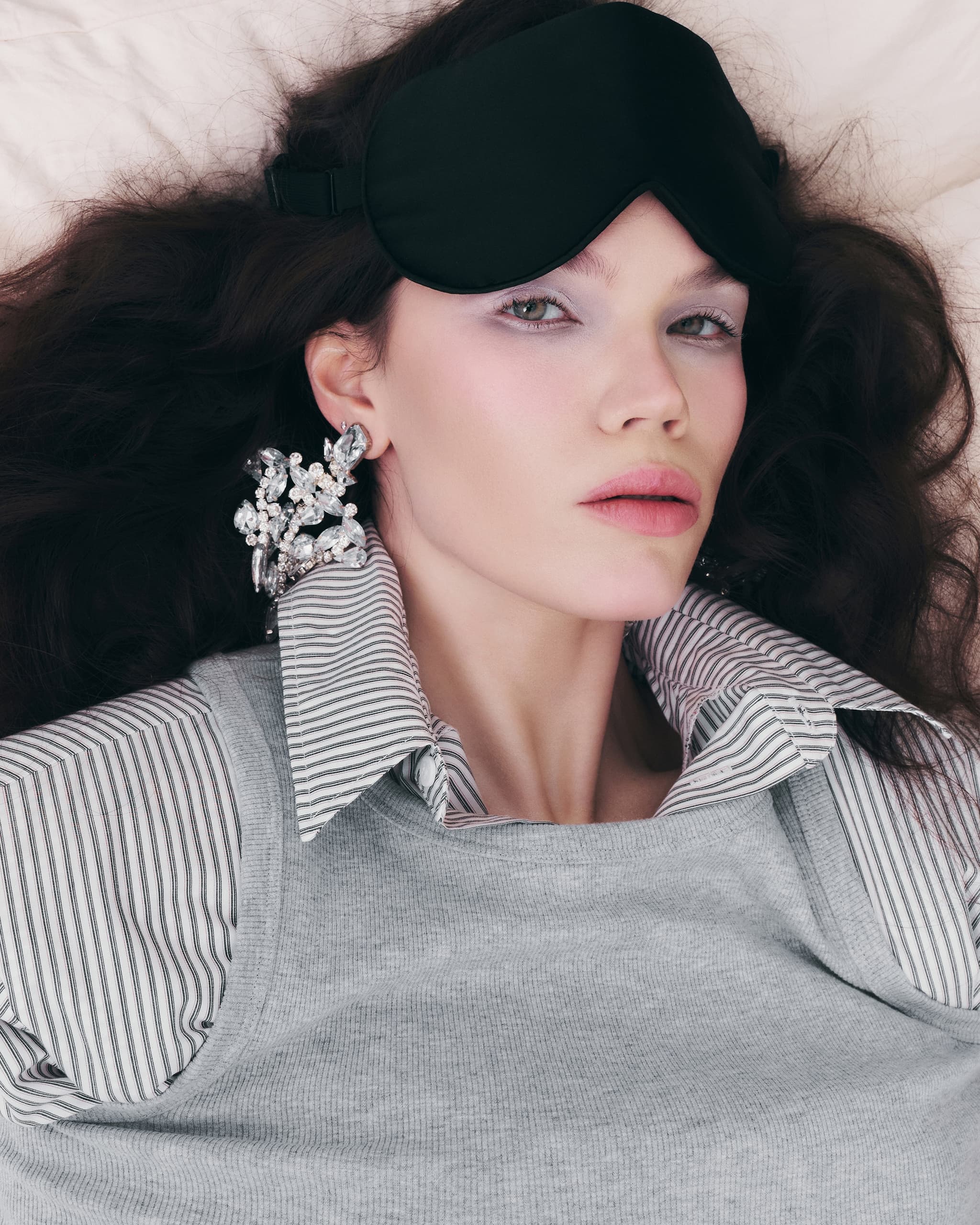 Woman in striped shirt wearing a sleep mask and statement crystal earrings.
