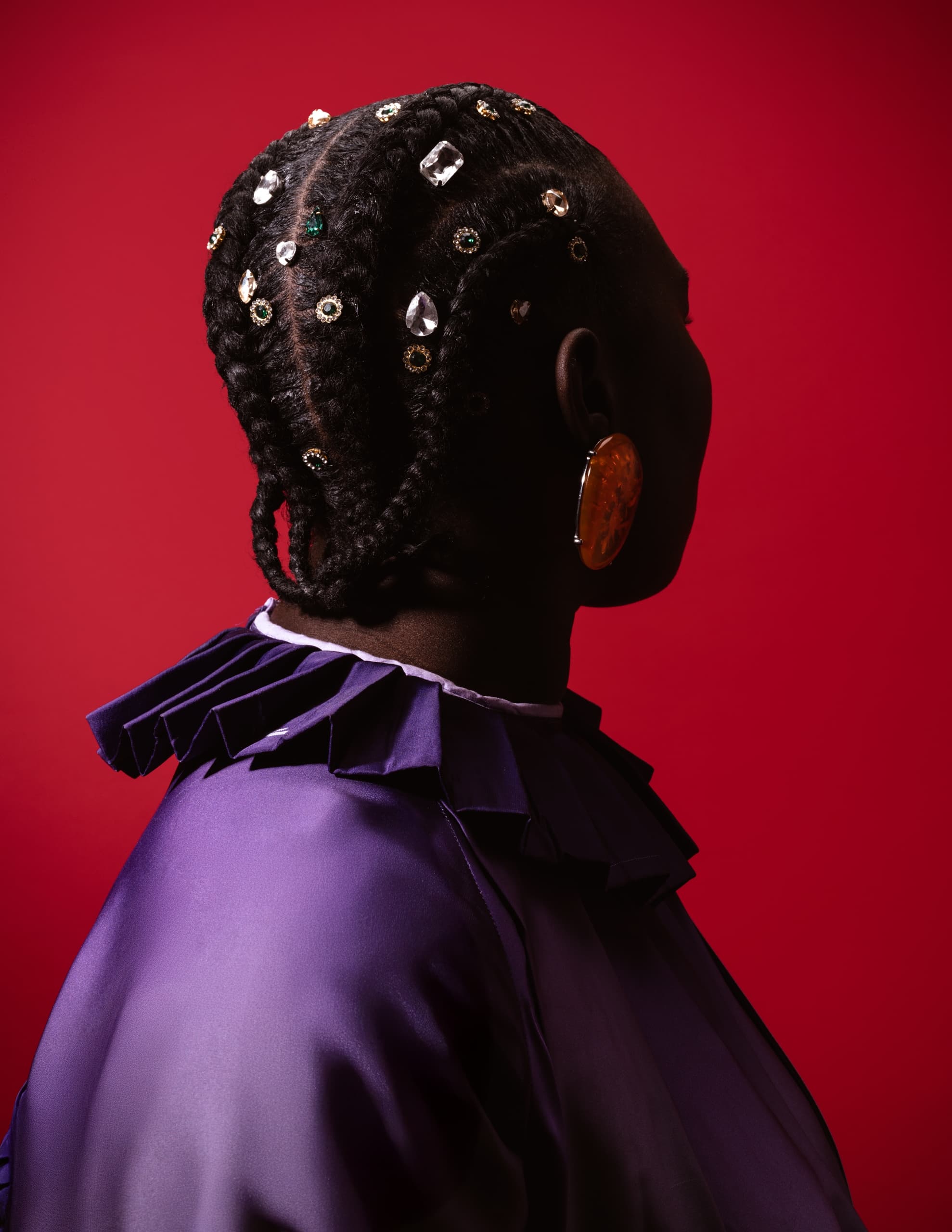Stylish braided hair with gems, purple outfit, red background. Fashion statement.