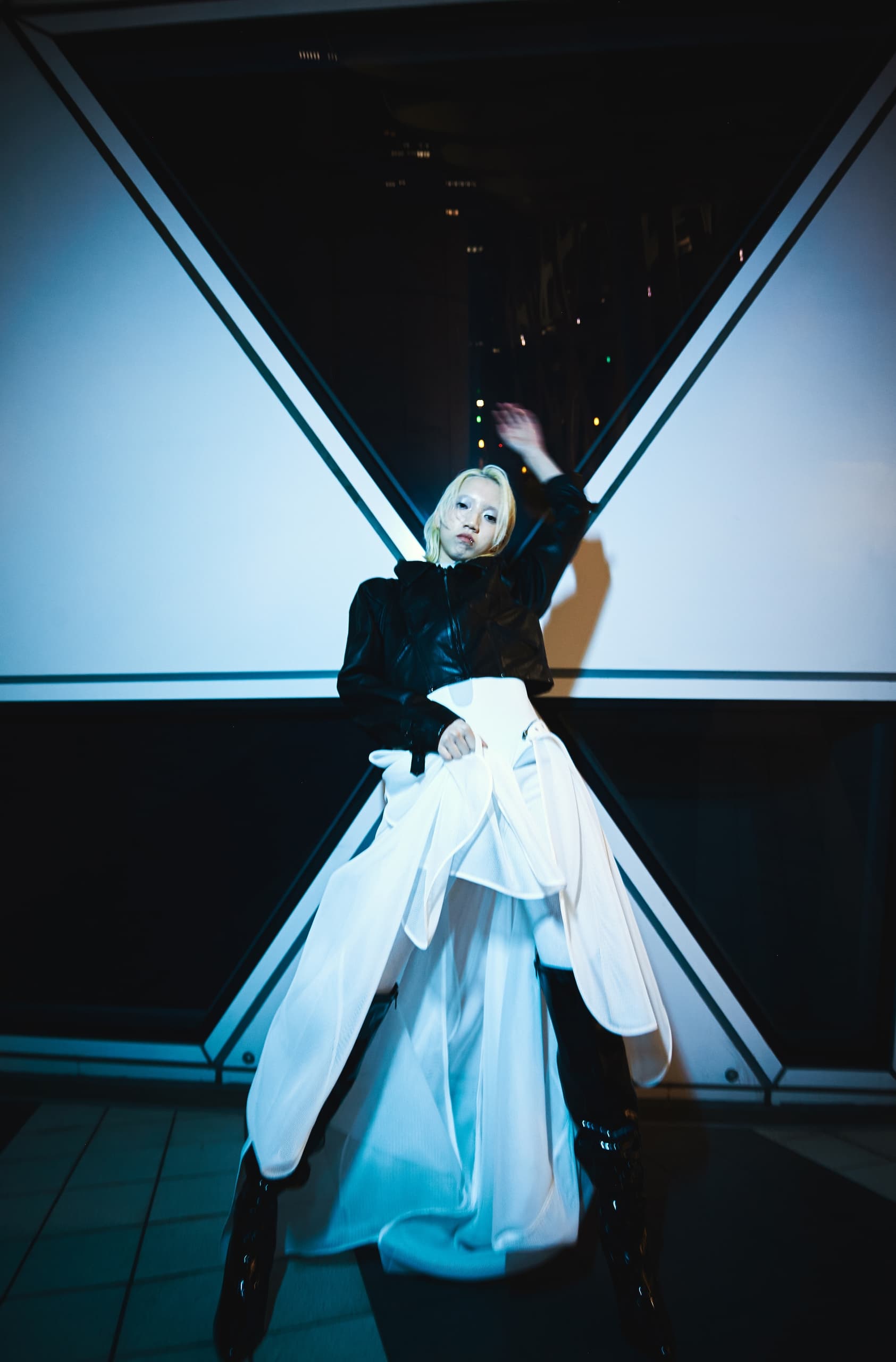 Fashionable model poses in black jacket and white dress at night.