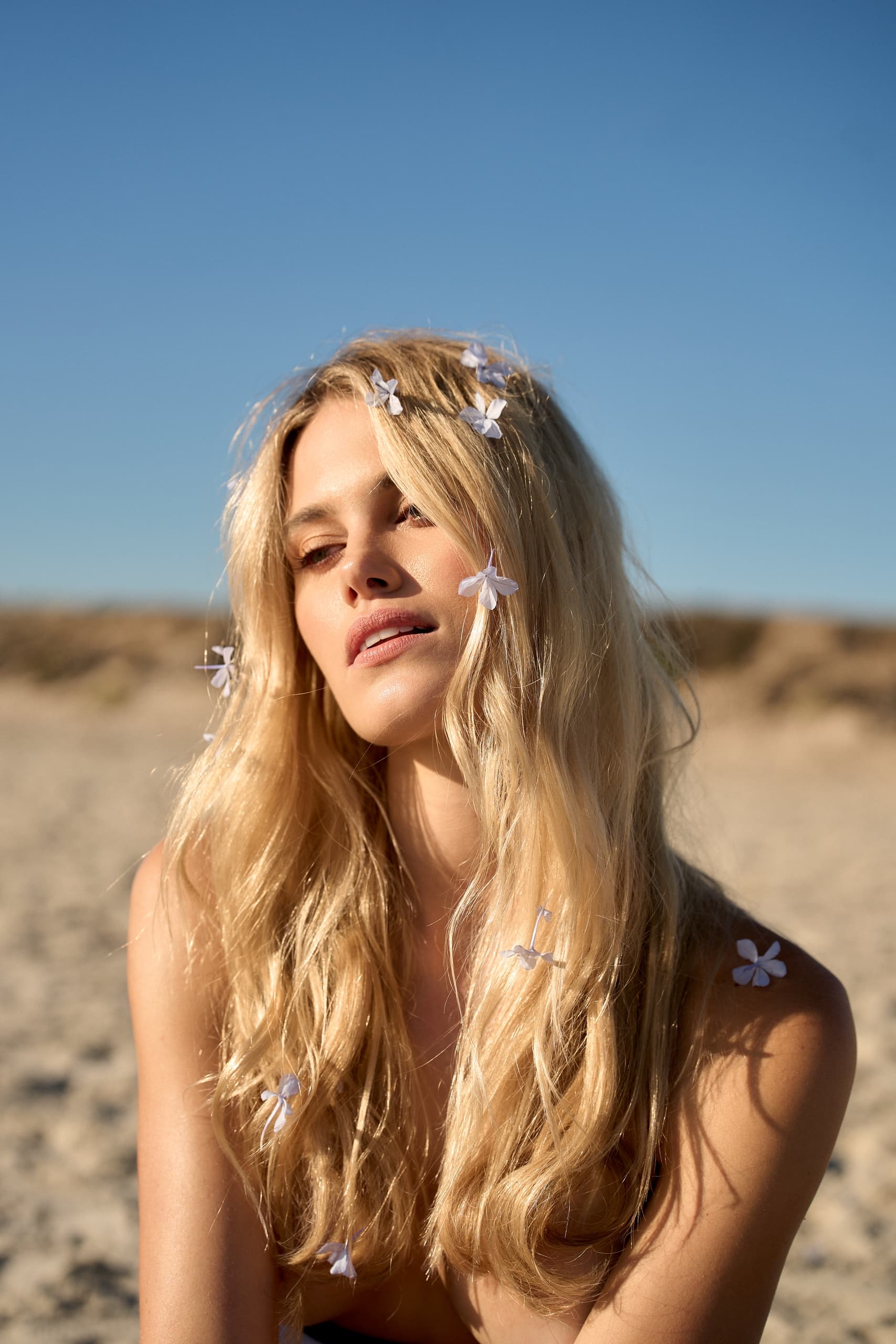 Woman with blonde hair and flowers on a sunny beach.