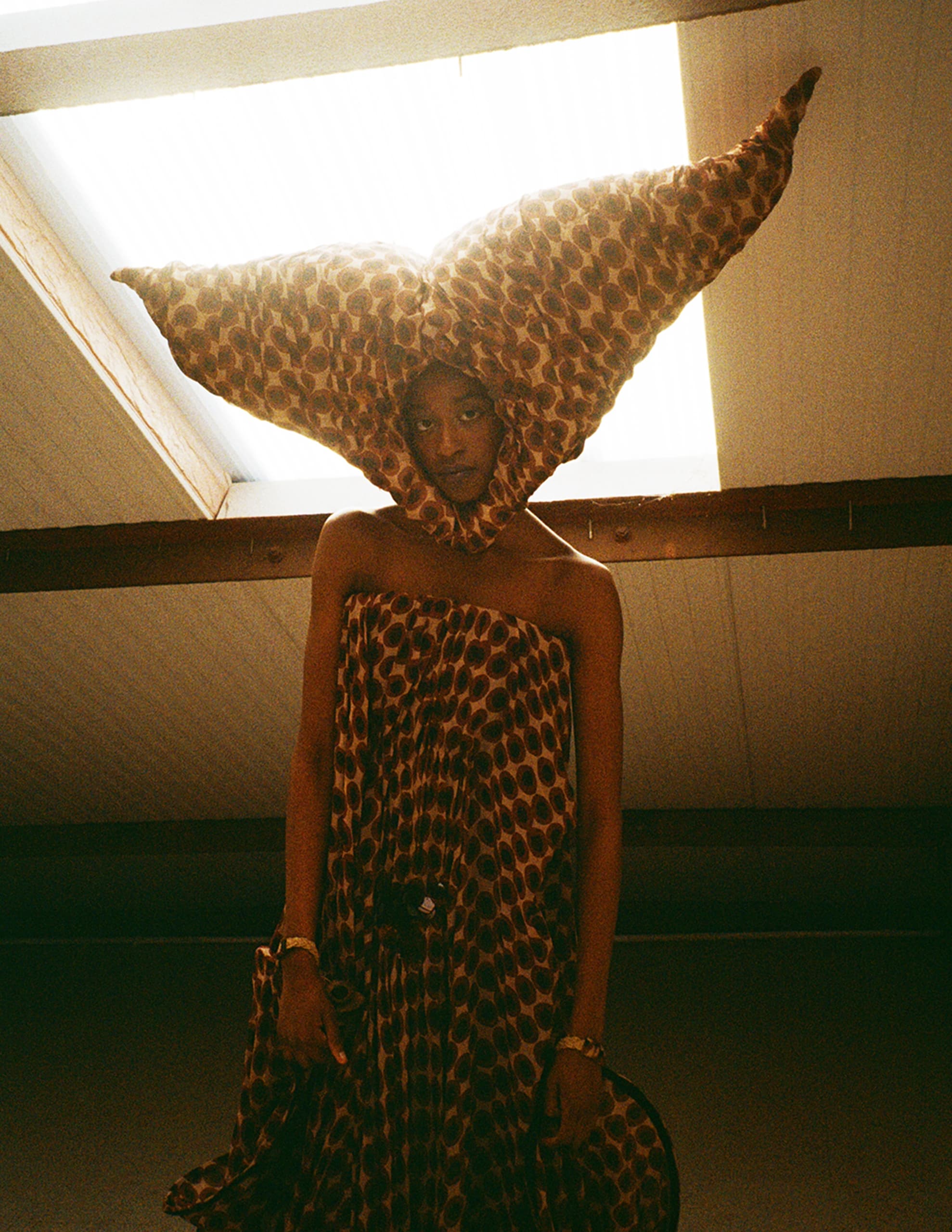 Person wearing artistic, patterned fabric in unique shape under skylight.
