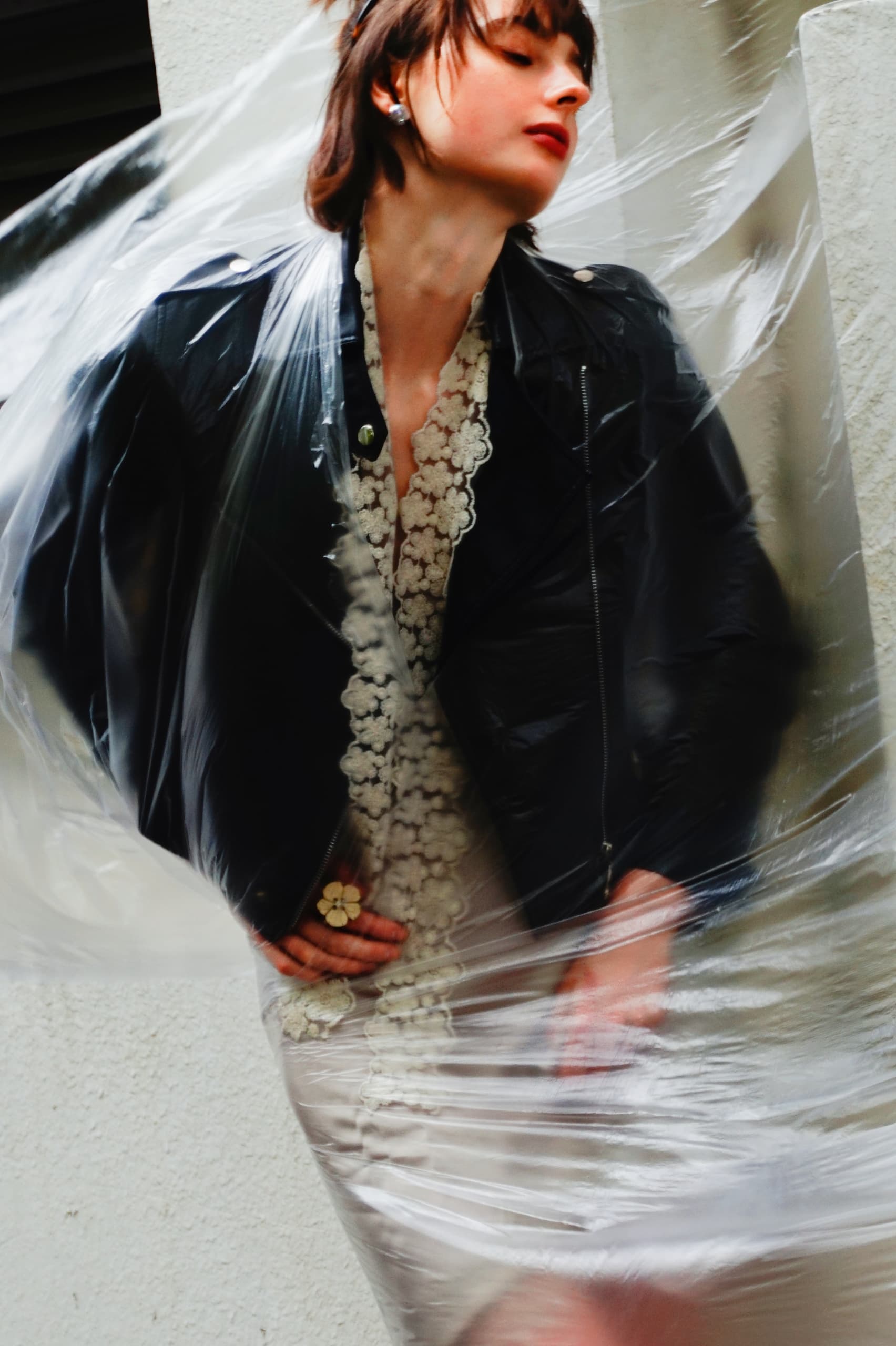 Fashionable woman in leather jacket and lace dress wrapped in translucent plastic.