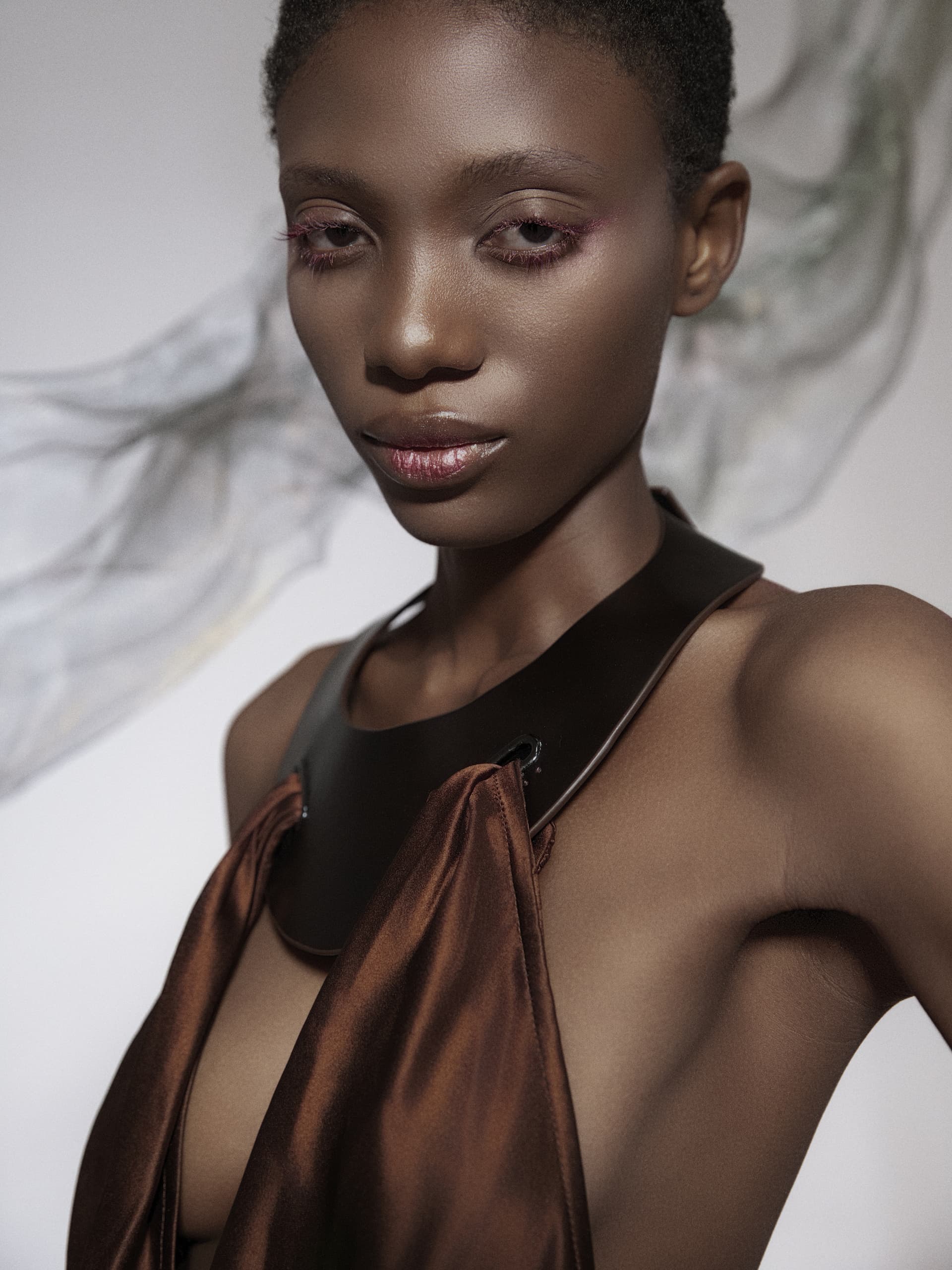 Fashion portrait of a person in a stylish brown dress with a flowing scarf.