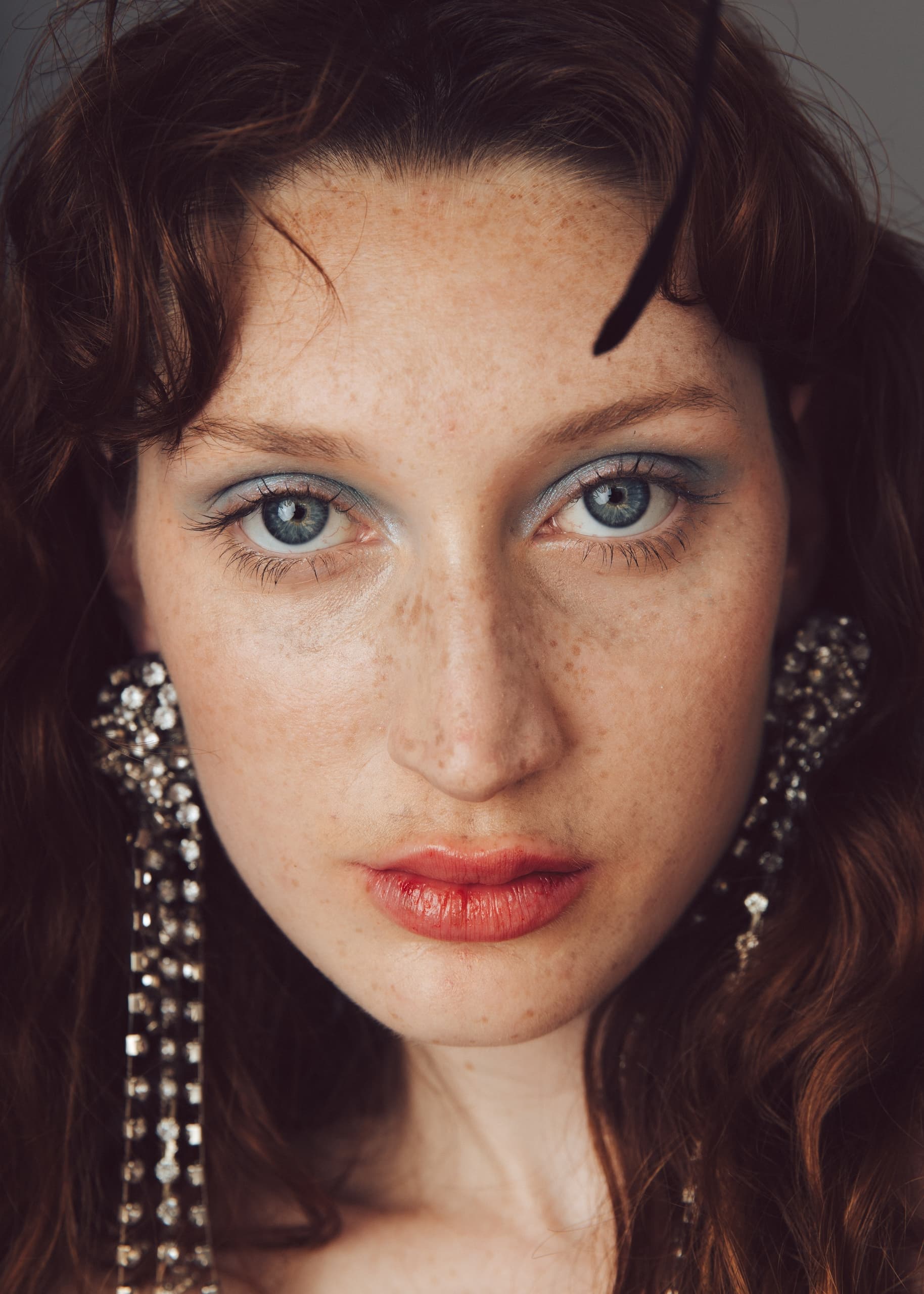 Close-up of a woman wearing sparkling earrings with vivid eye makeup.