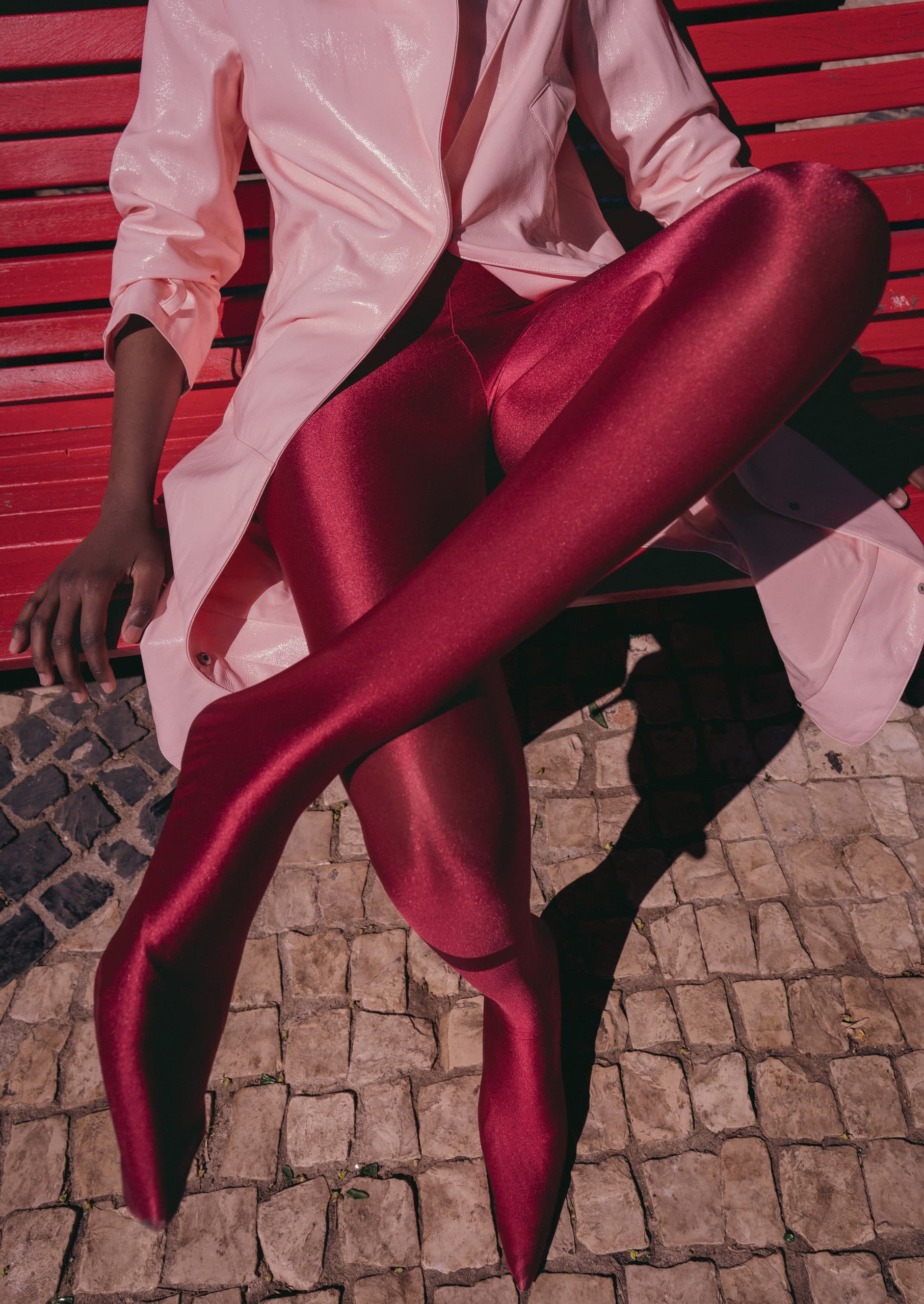 Fashionable woman in red tights and pink coat sitting on a red bench.
