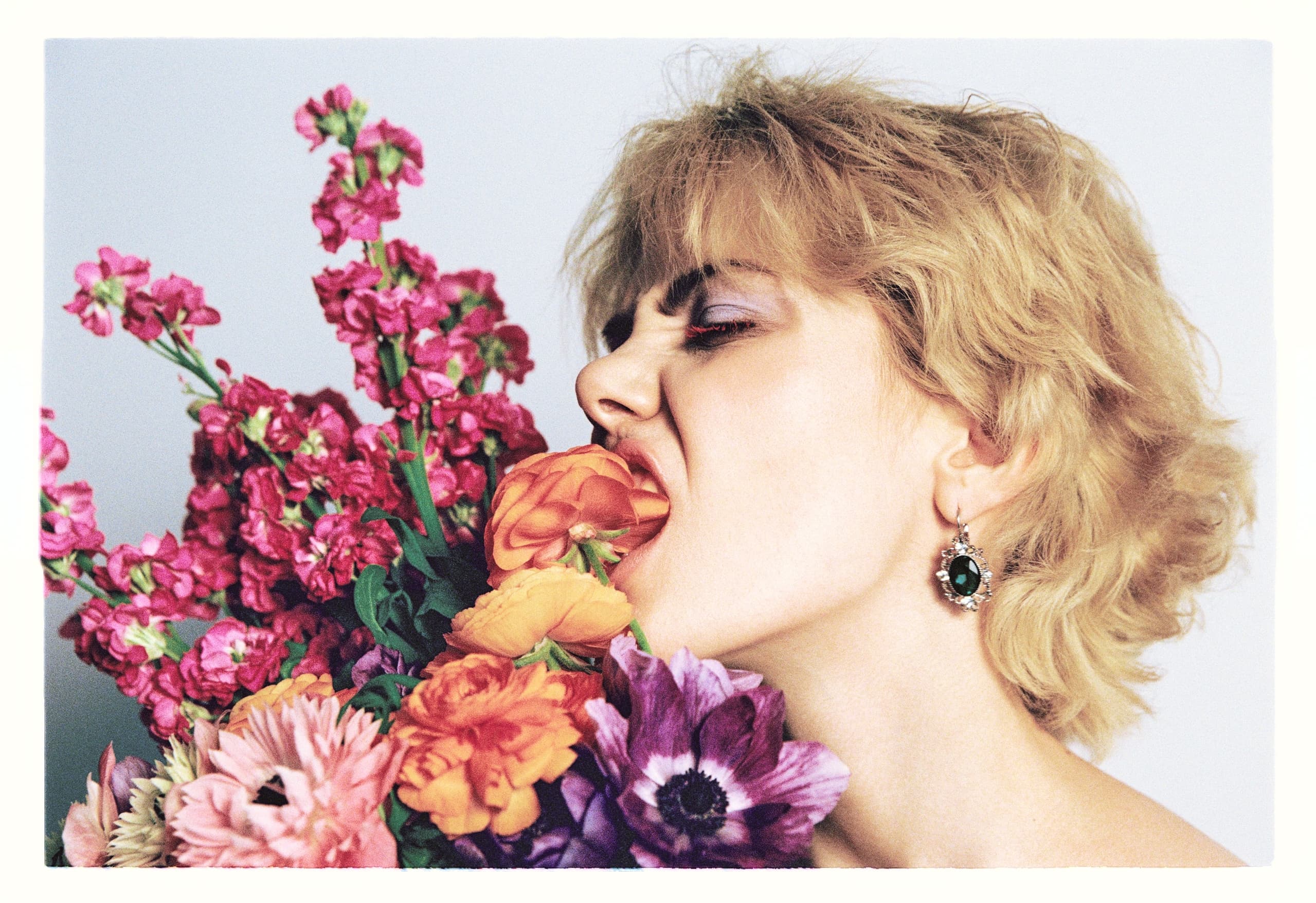 Person playfully biting colorful flowers against a light background.