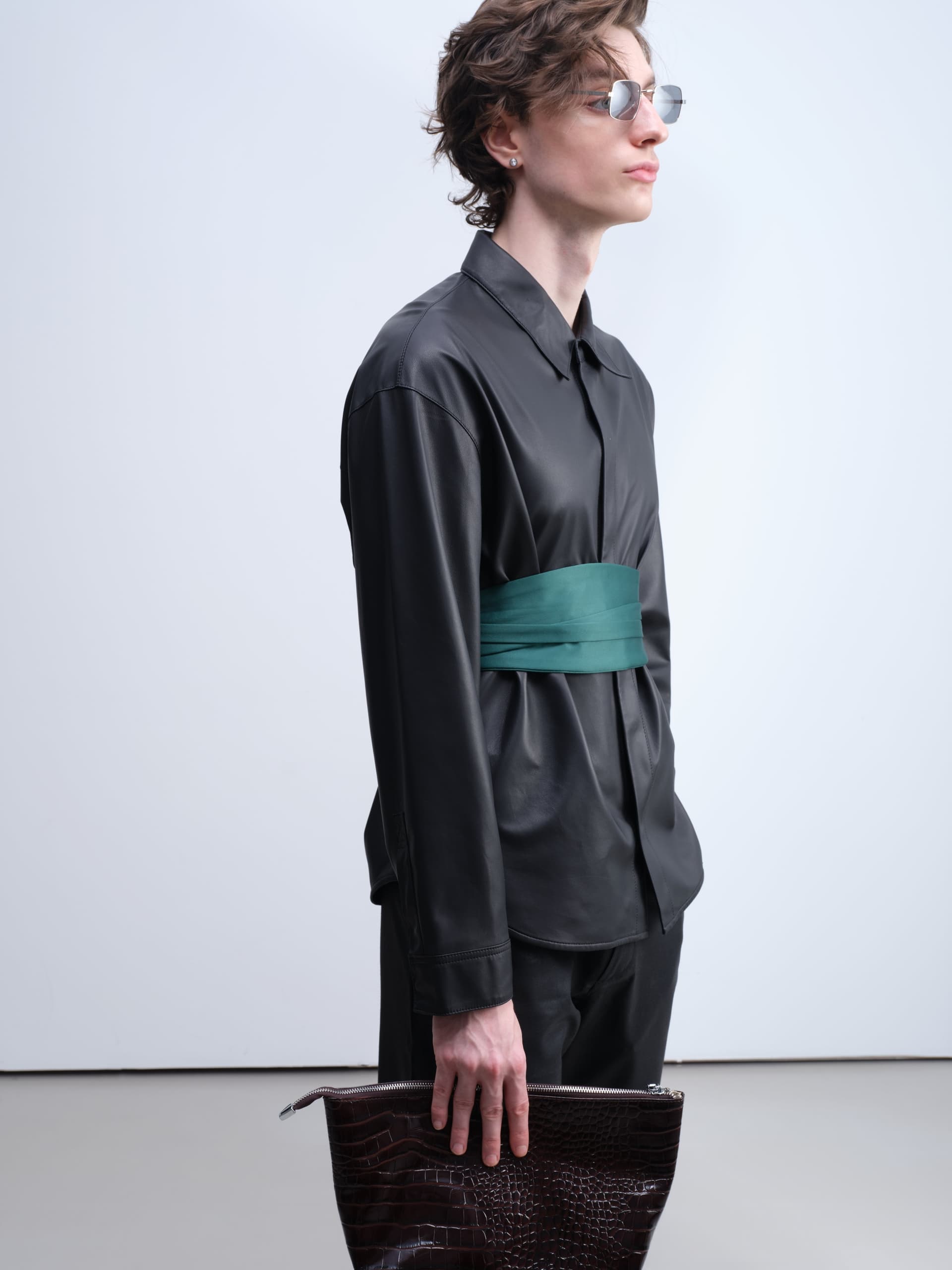 Person in stylish black leather outfit with green belt and holding a brown textured clutch