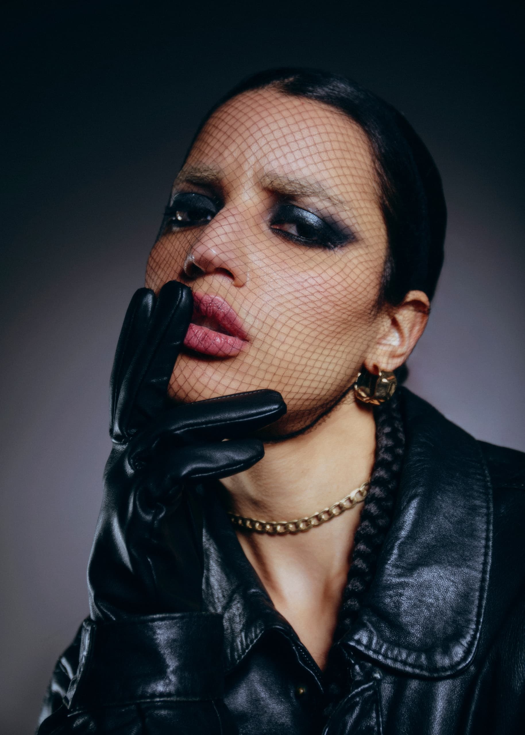 Woman in leather jacket and gloves, wearing fishnet veil and bold makeup.