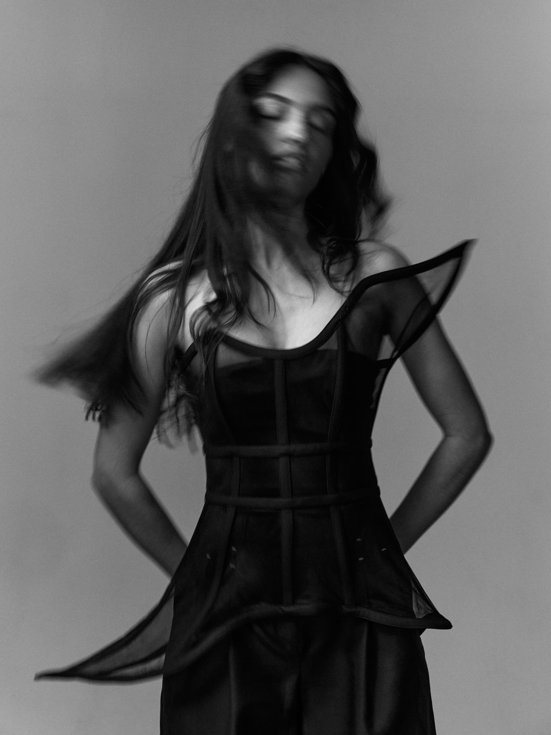 Black and white photo of a woman in a flowing, structured dress with motion blur.