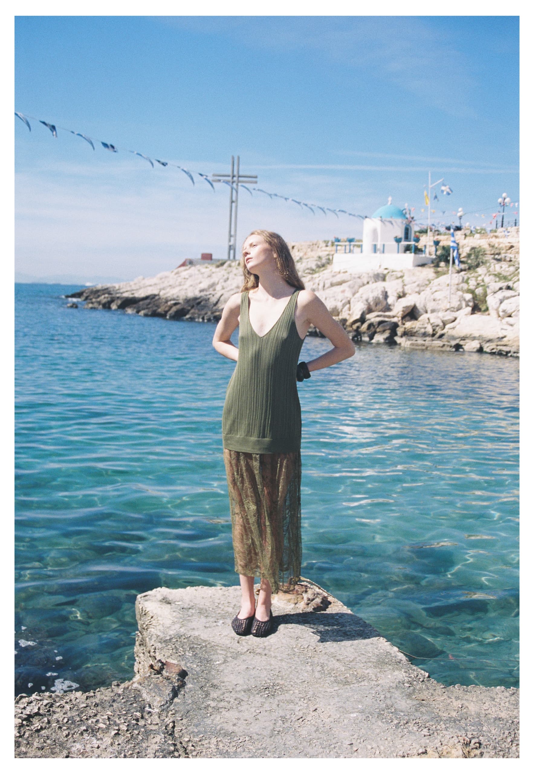 Woman in green dress stands by ocean with blue sky background.