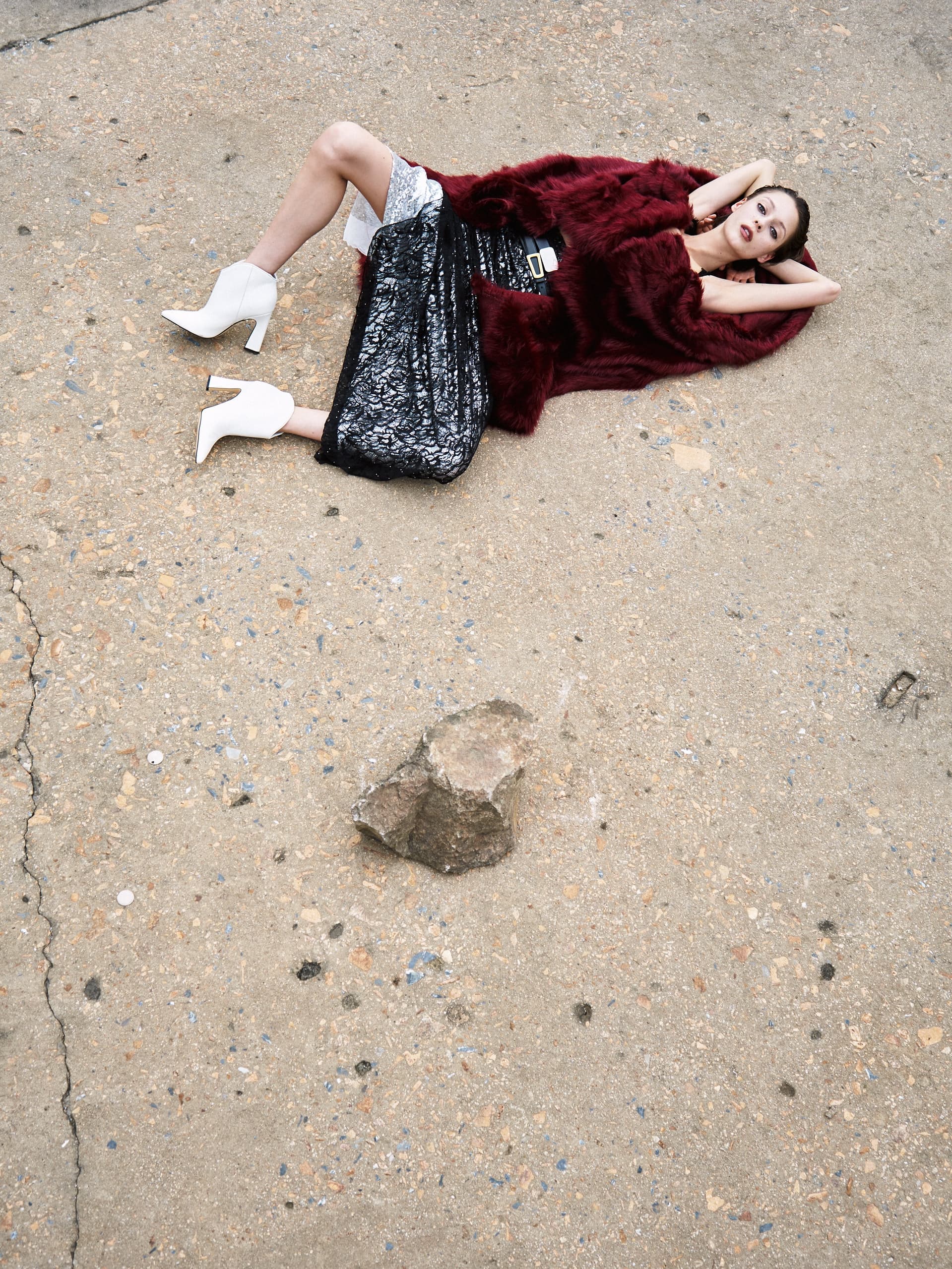 Fashion model in luxurious outfit poses creatively on textured ground.