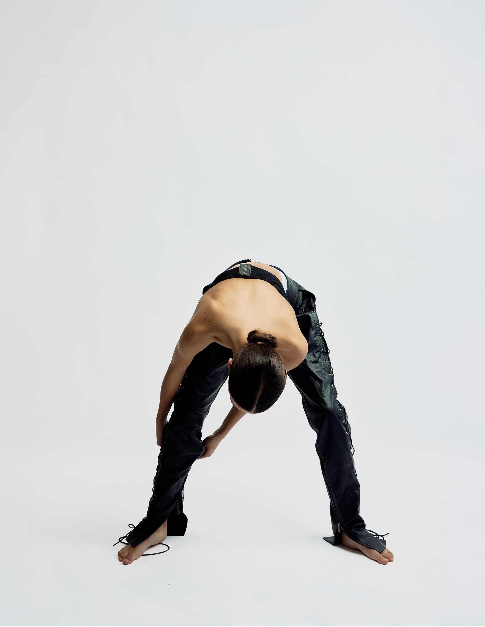Person in black pants bending forward, minimalist setting, fashion pose.
