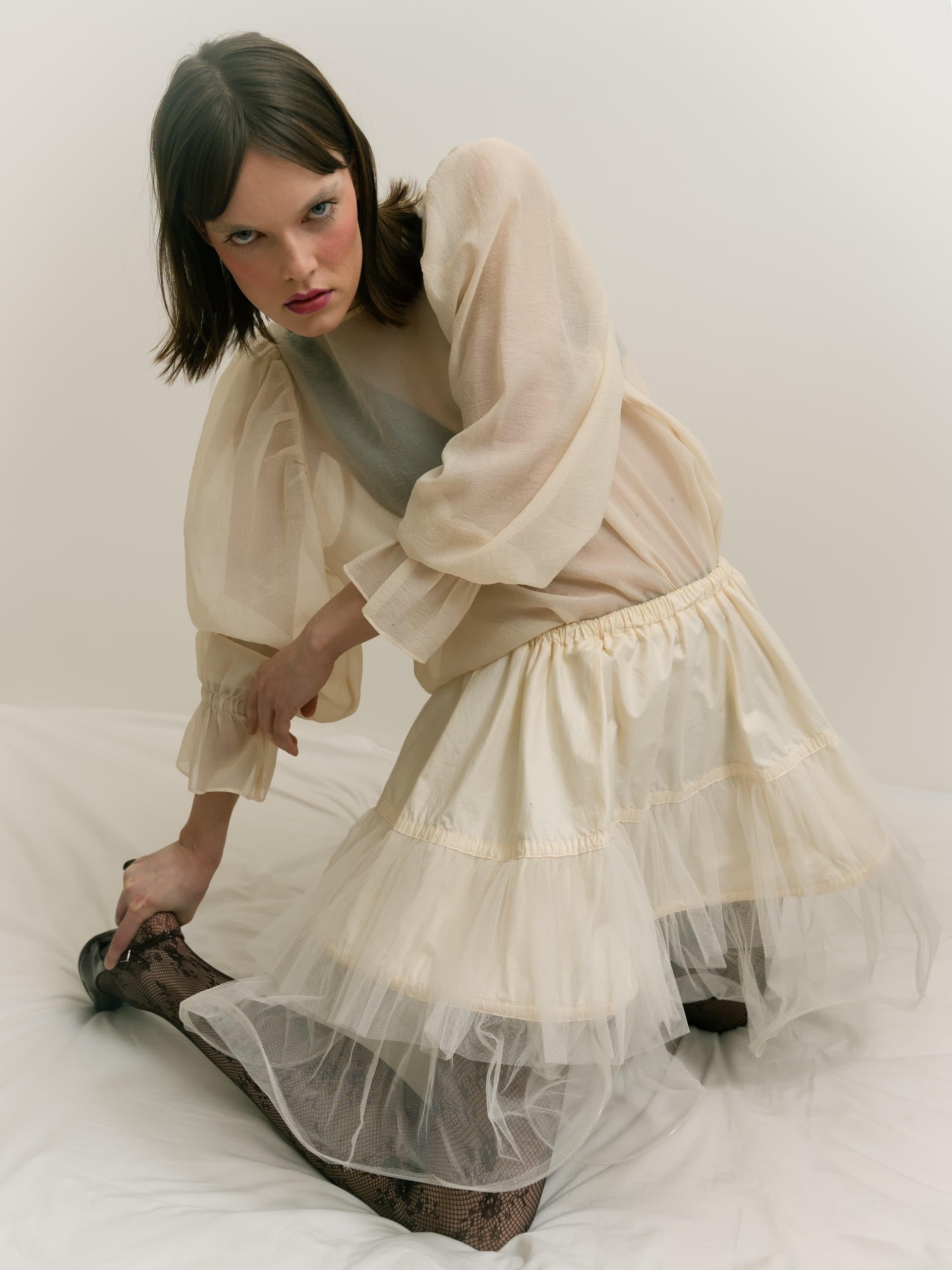 Woman in vintage sheer dress posing elegantly on white background.