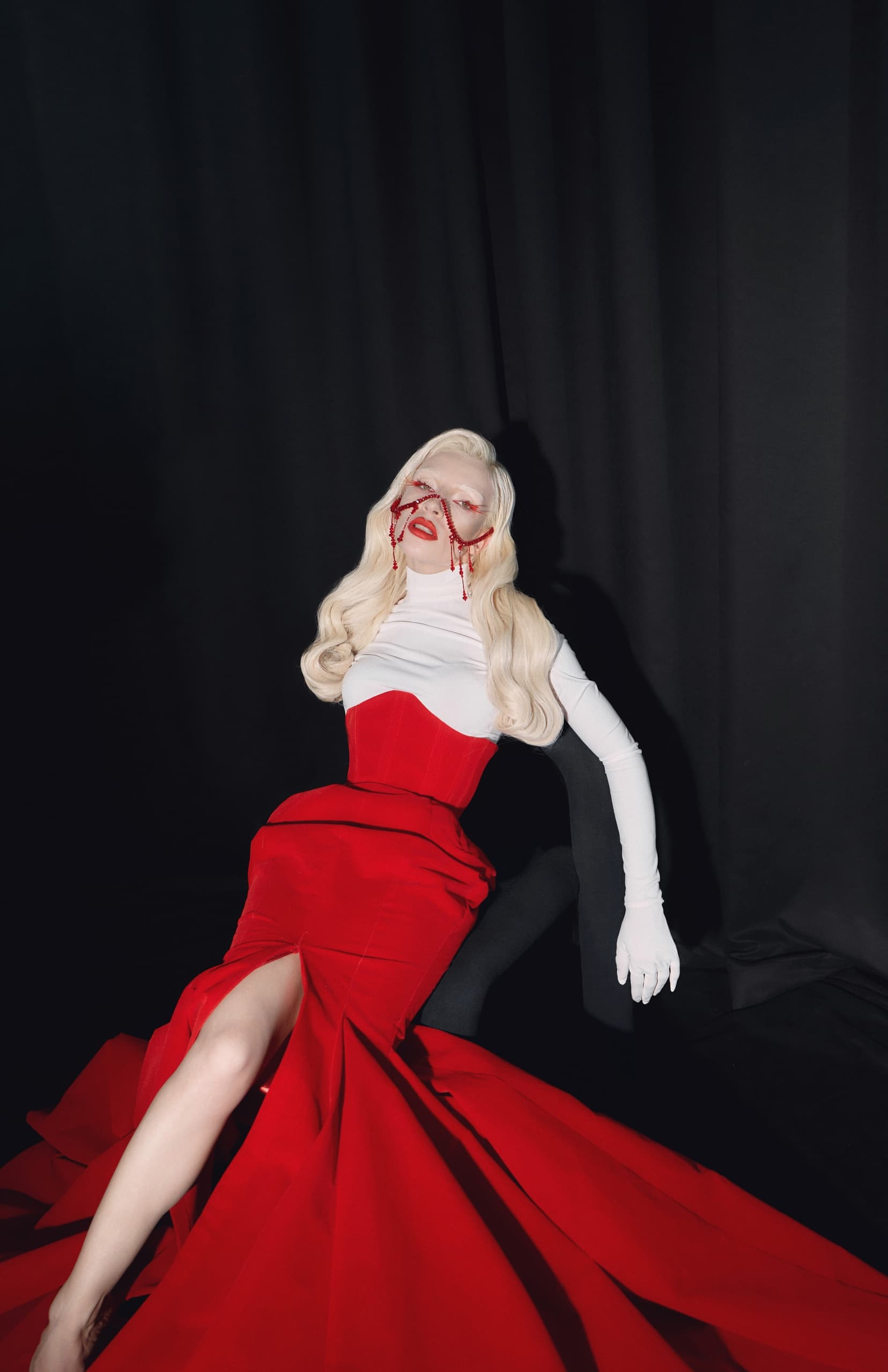 Striking woman in a red and white gown with bold accessories against a dark backdrop.