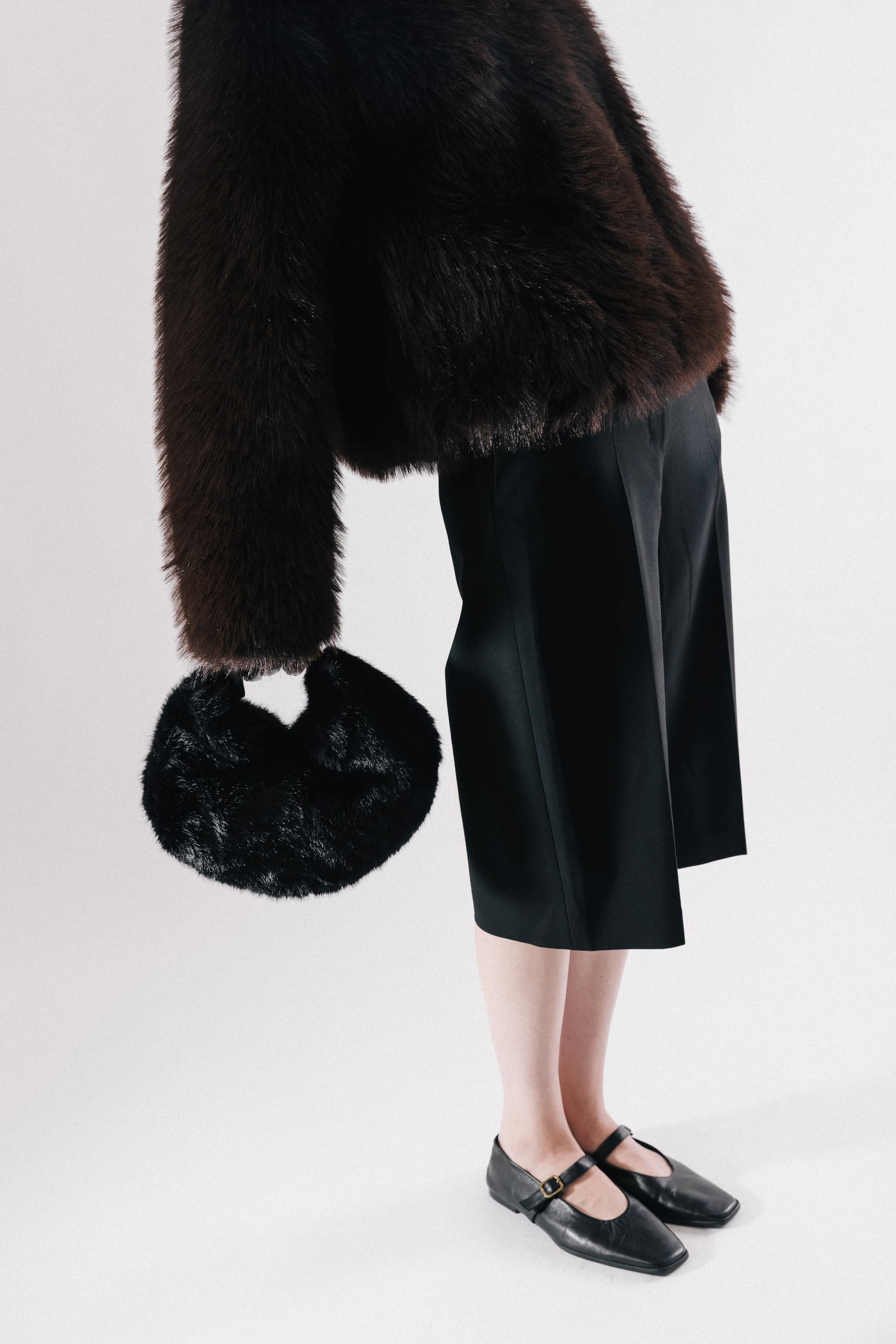 Fashionable outfit with fur coat, black skirt, stylish shoes, and a plush handbag.