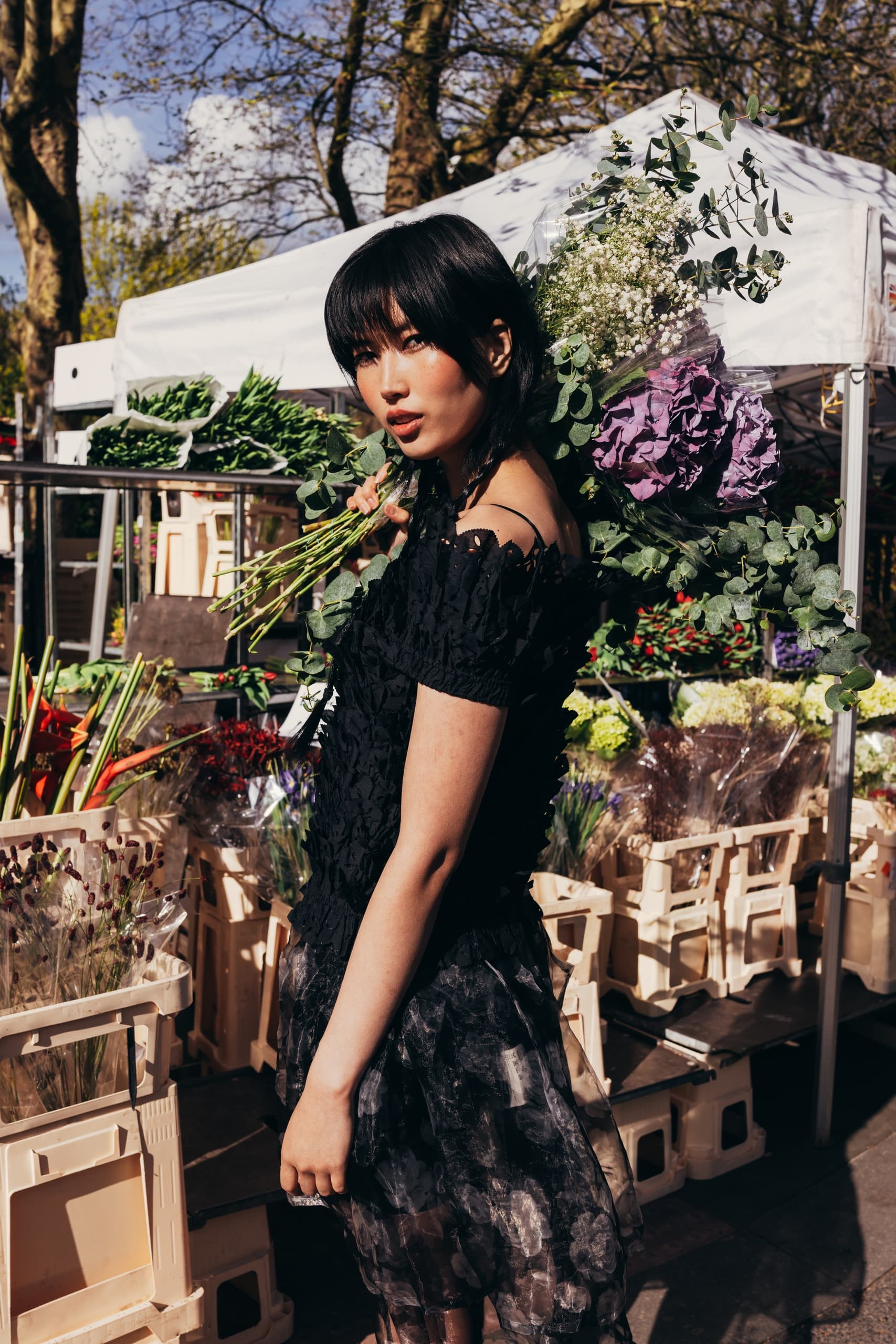 Woman with bouquet at outdoor flower market in stylish black dress.