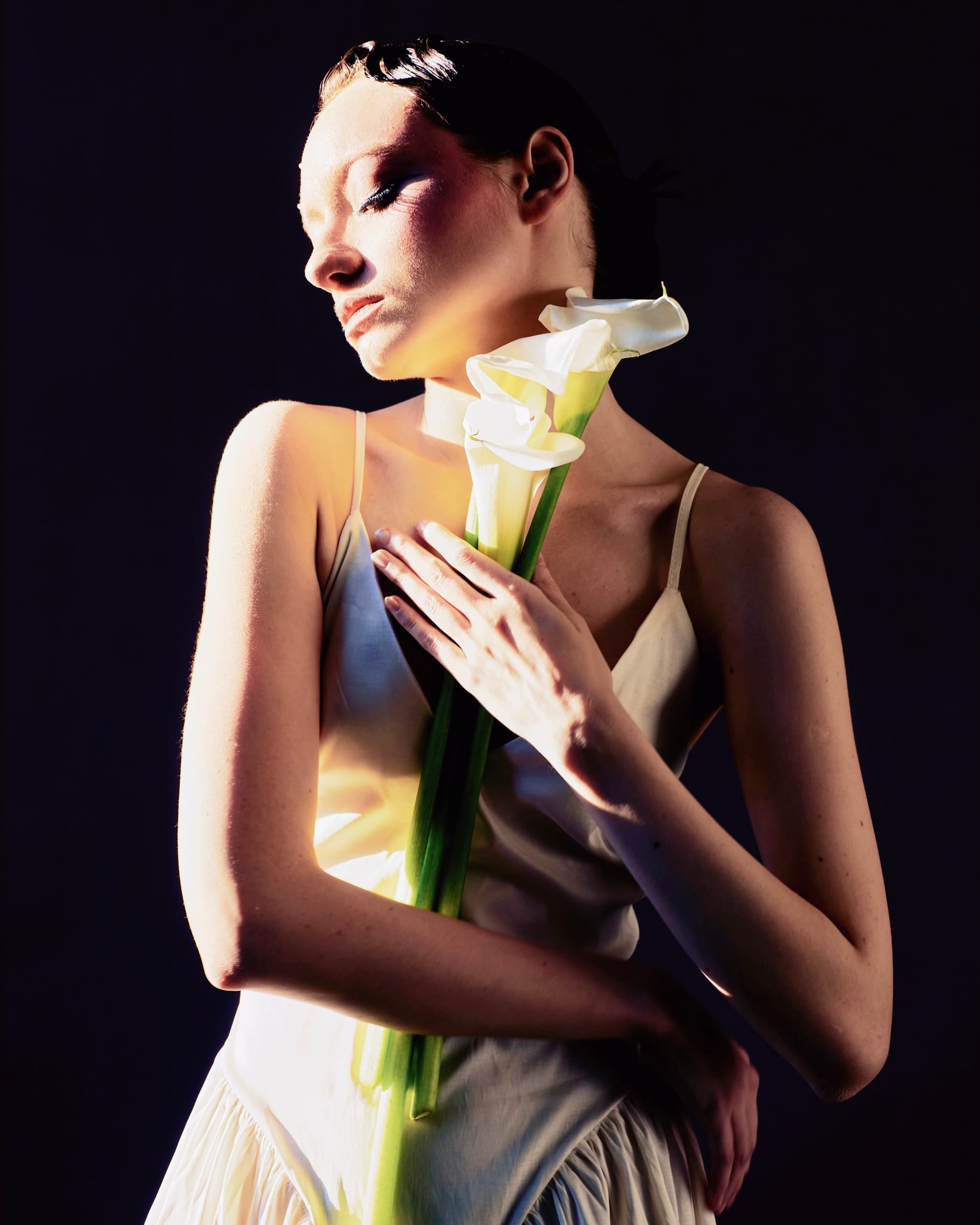 Woman holding white calla lilies in dramatic lighting, elegant and serene portrait.