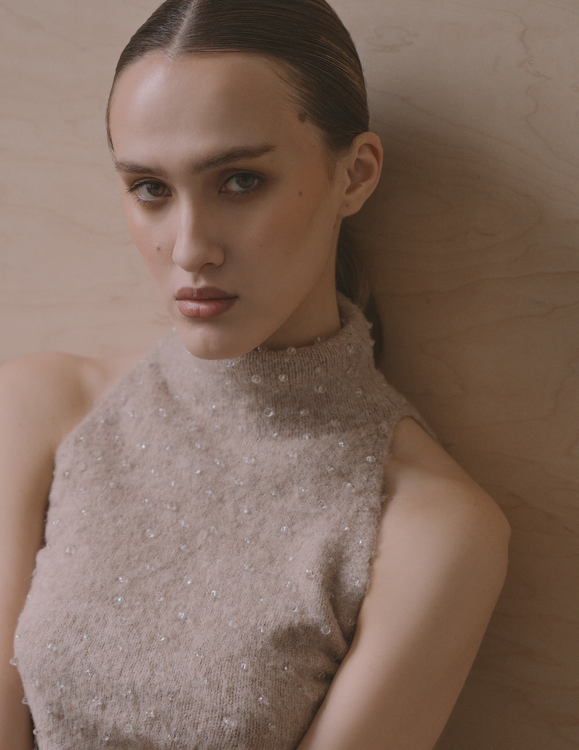 Woman in textured beige top against wooden backdrop.