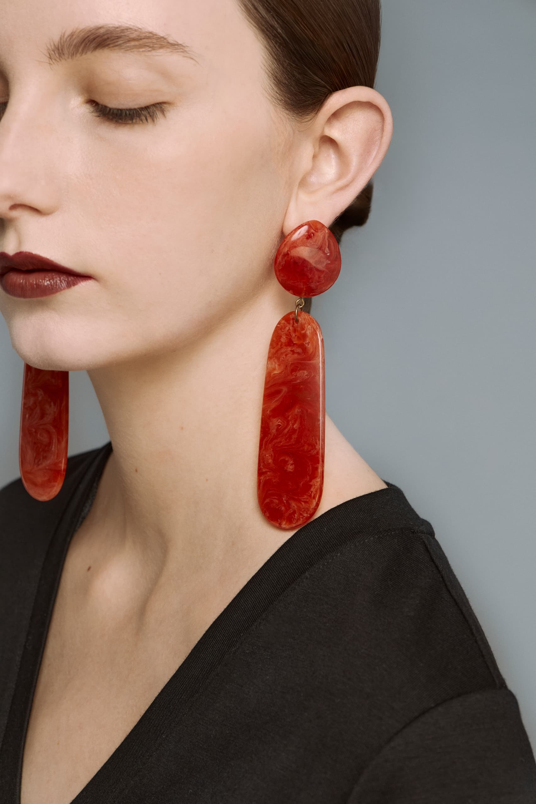 Woman wearing bold red statement earrings against a neutral backdrop.