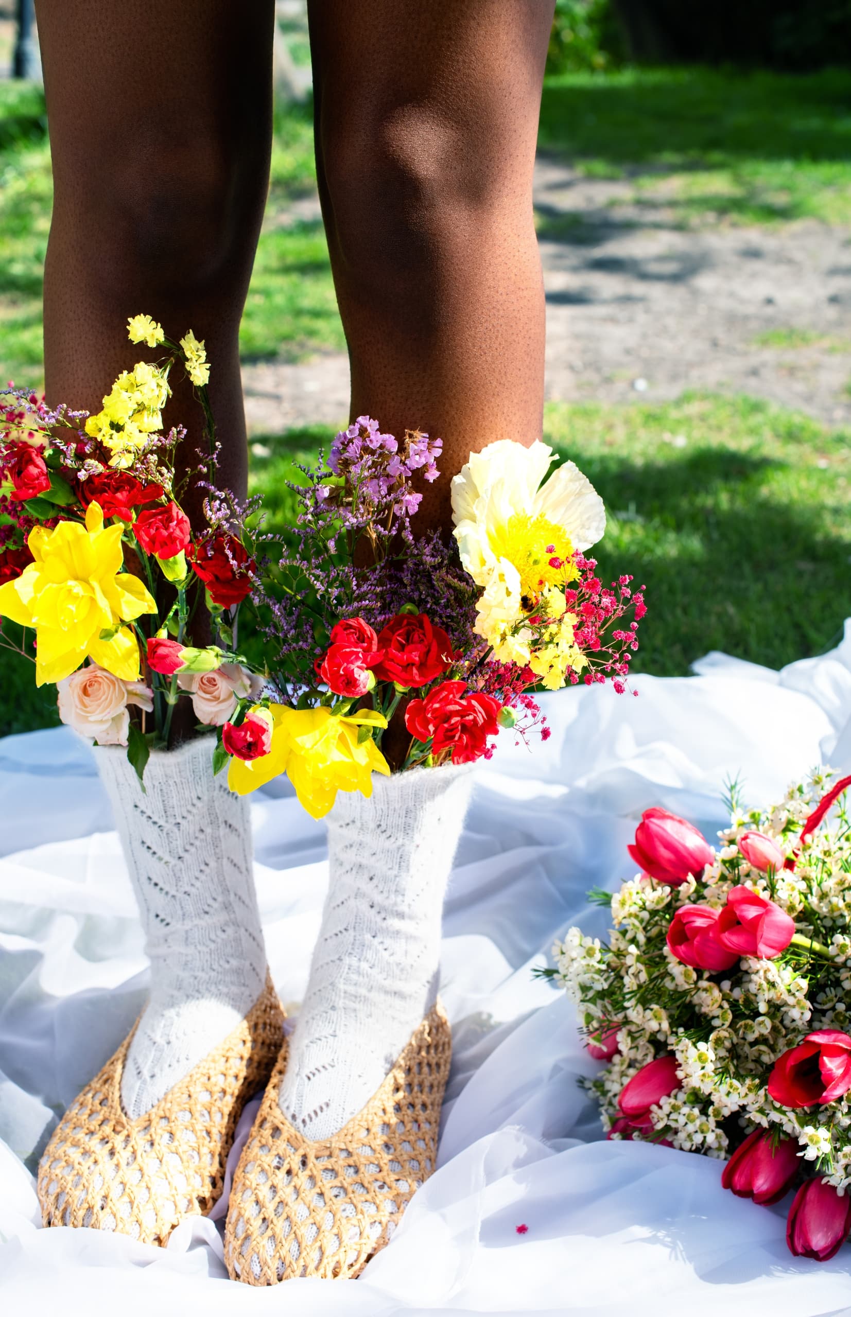 Person wearing woven shoes with flowers tucked in, standing on a white cloth.