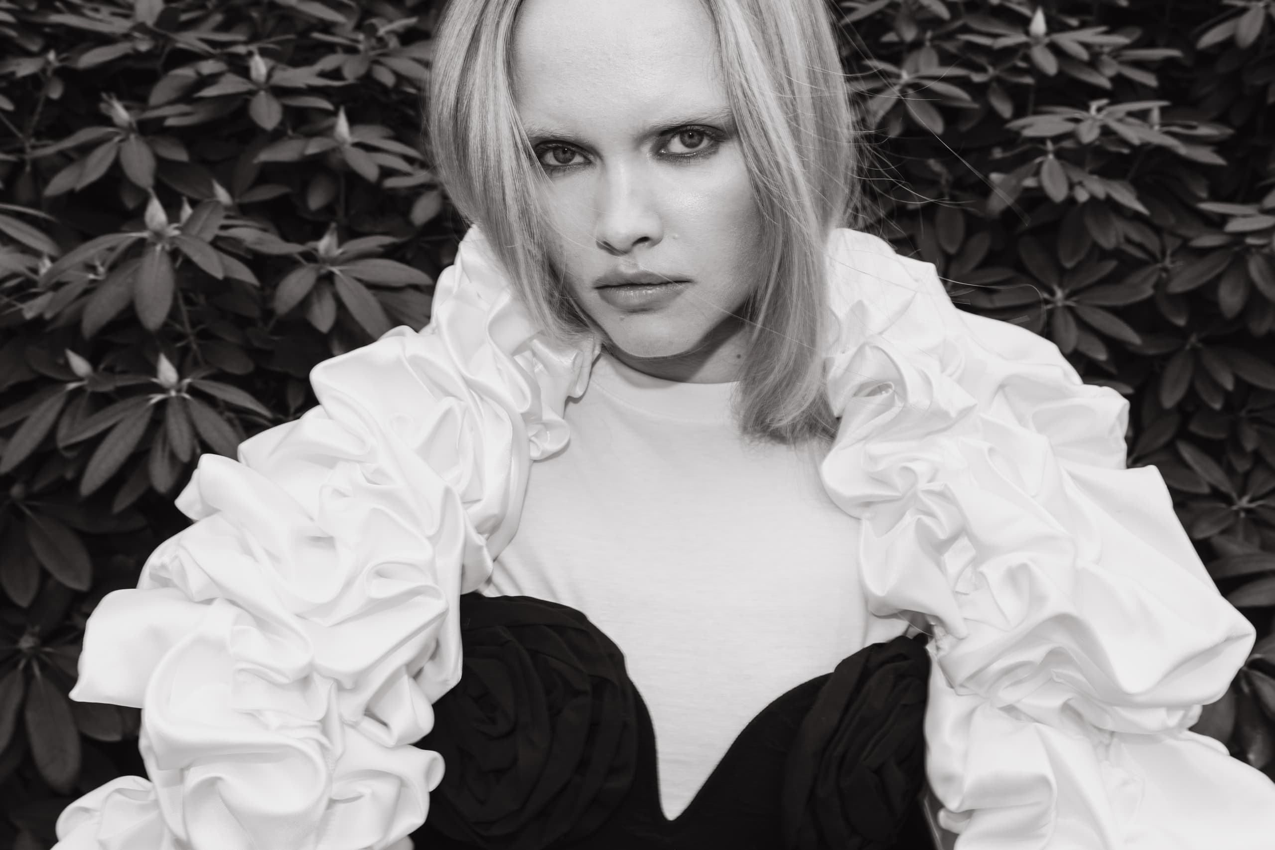 Woman in elegant attire against a leafy backdrop, showcasing fashion style.